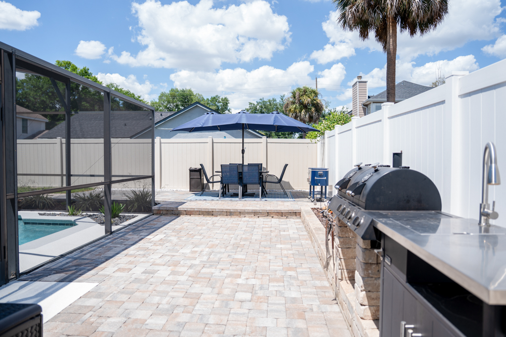 Backyard patio with outdoor kitchen, grill and dining set under umbrella