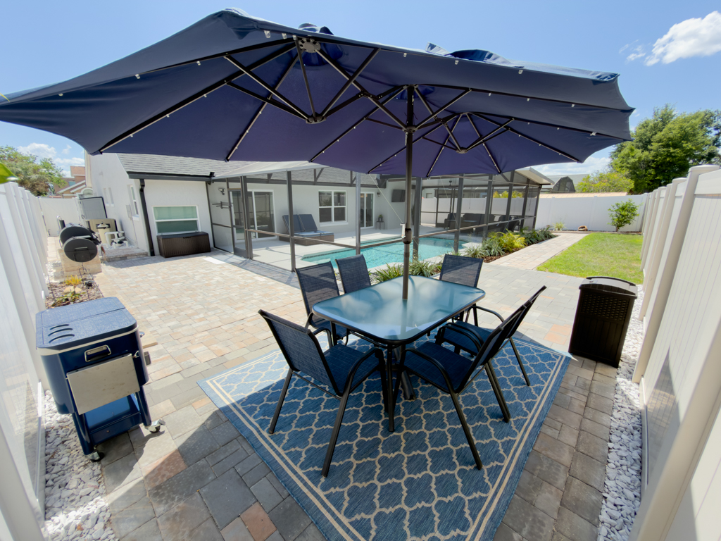 Backyard paver patio with dining table, umbrella and view to pool enclosure