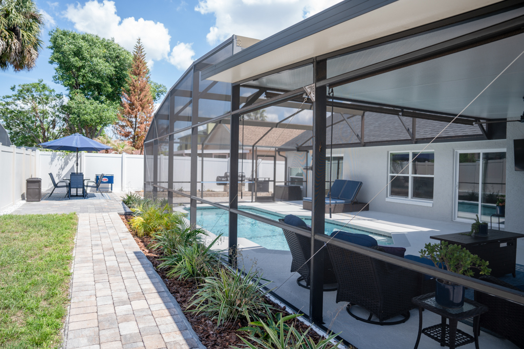 Exterior view of pool enclosure, paver walkway and backyard landscaping