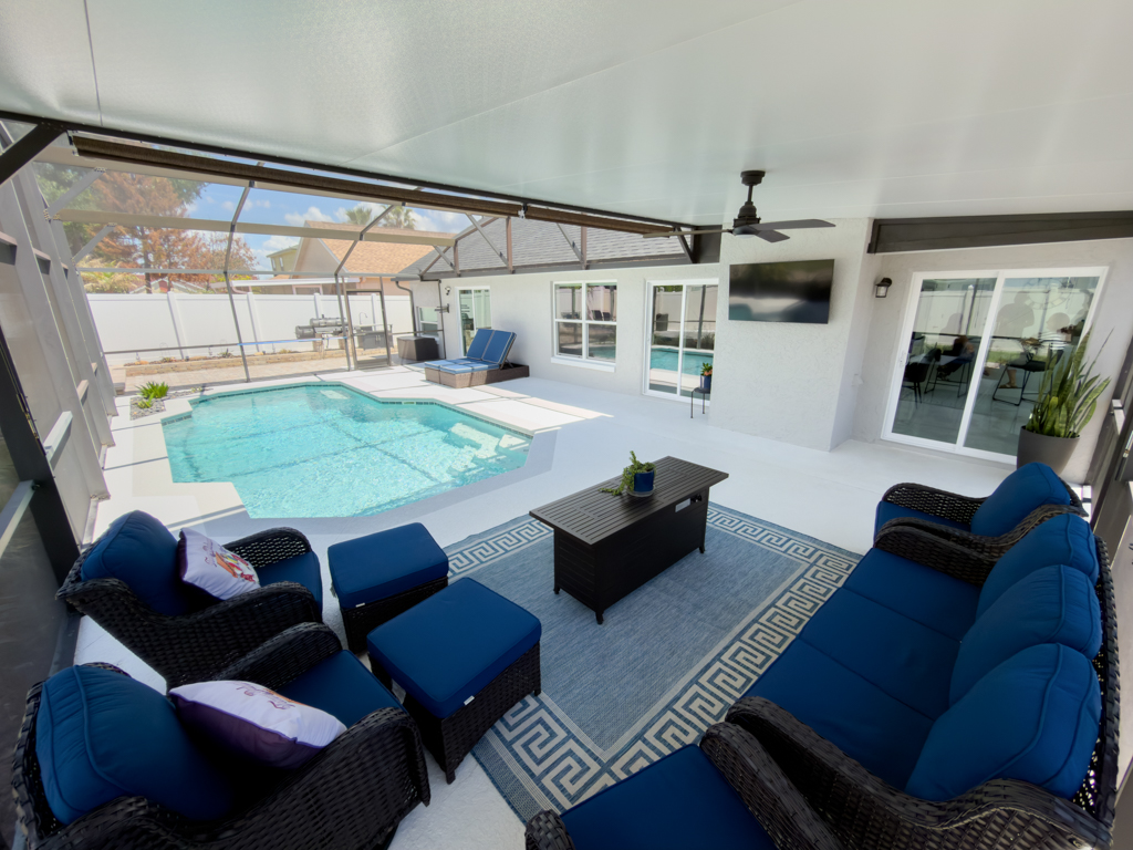 Covered lanai with blue outdoor seating set, fire pit table and pool view