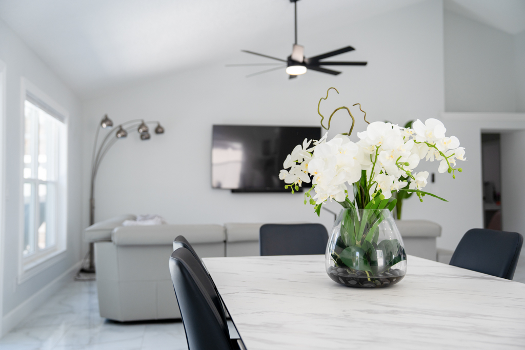 Close-up detail of dining table with white orchid centerpiece and living room in background