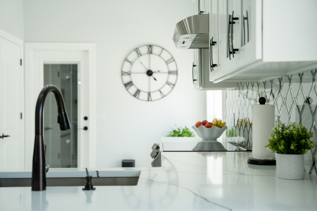 Close-up kitchen counter detail with faucet, mirror backsplash and fruit bowl