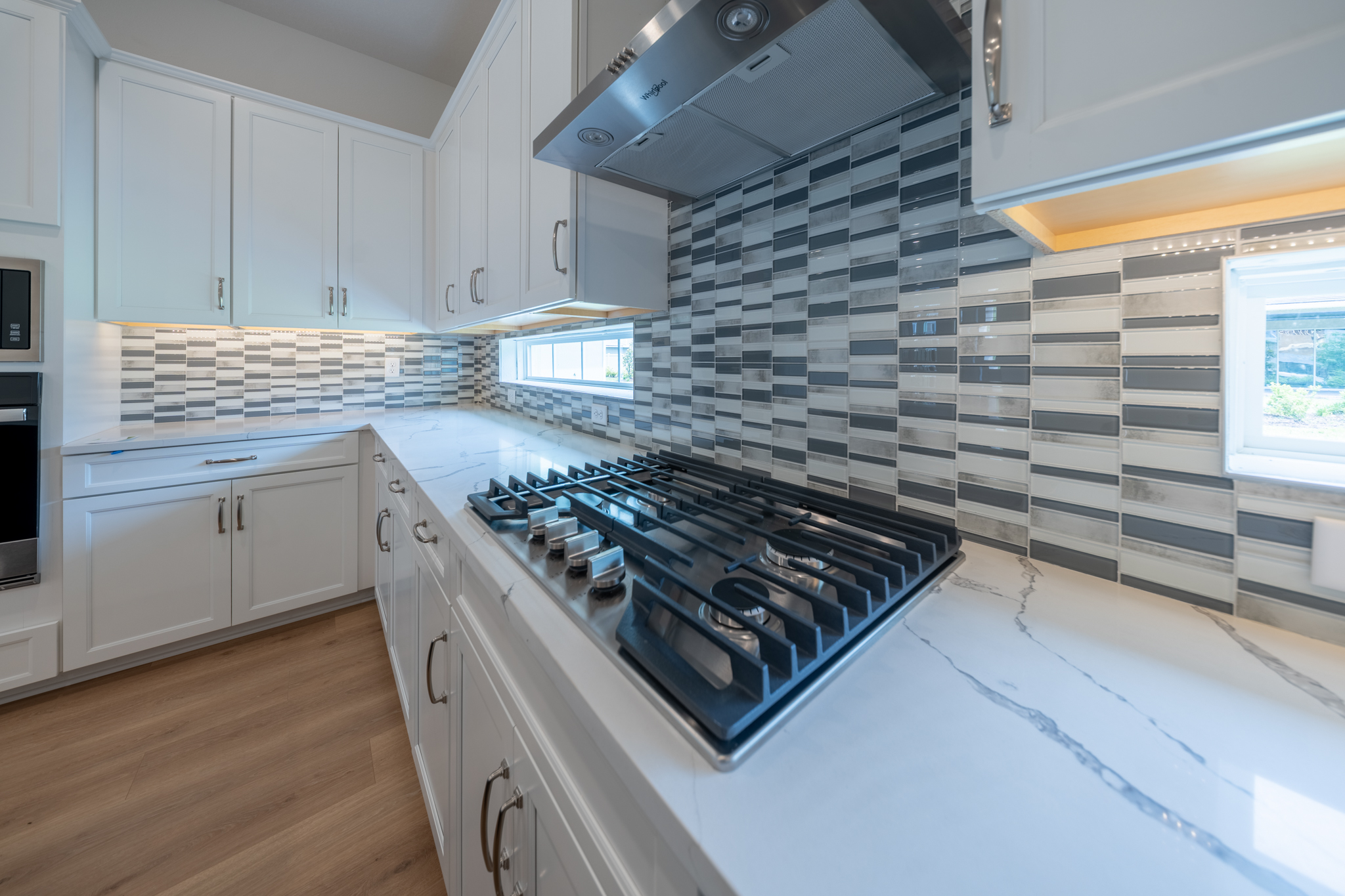 Kitchen detail with gas cooktop, mosaic tile backsplash, stainless range hood and quartz counters