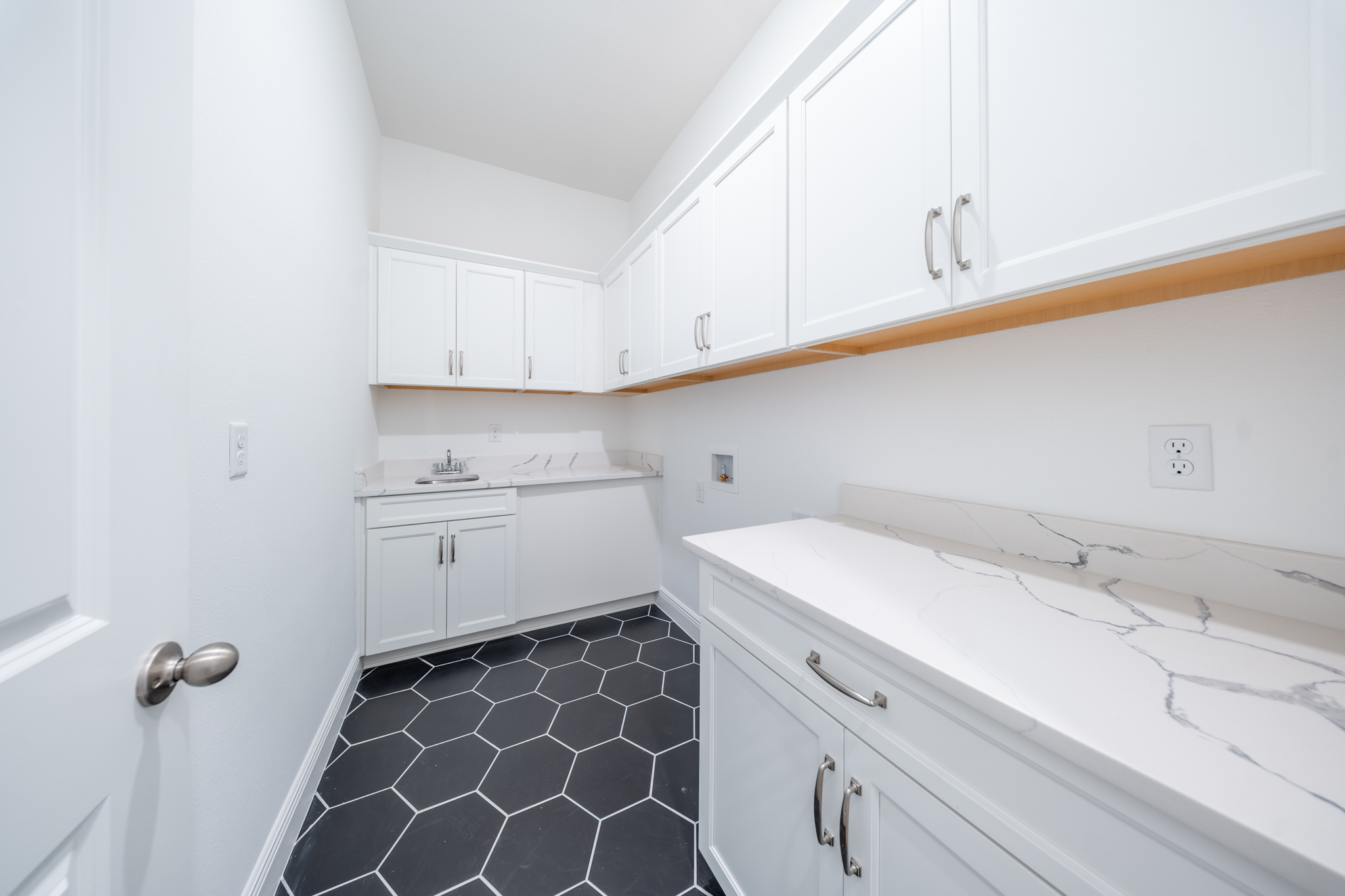 Laundry room with white cabinetry, quartz counters, utility sink and black hexagon tile floor