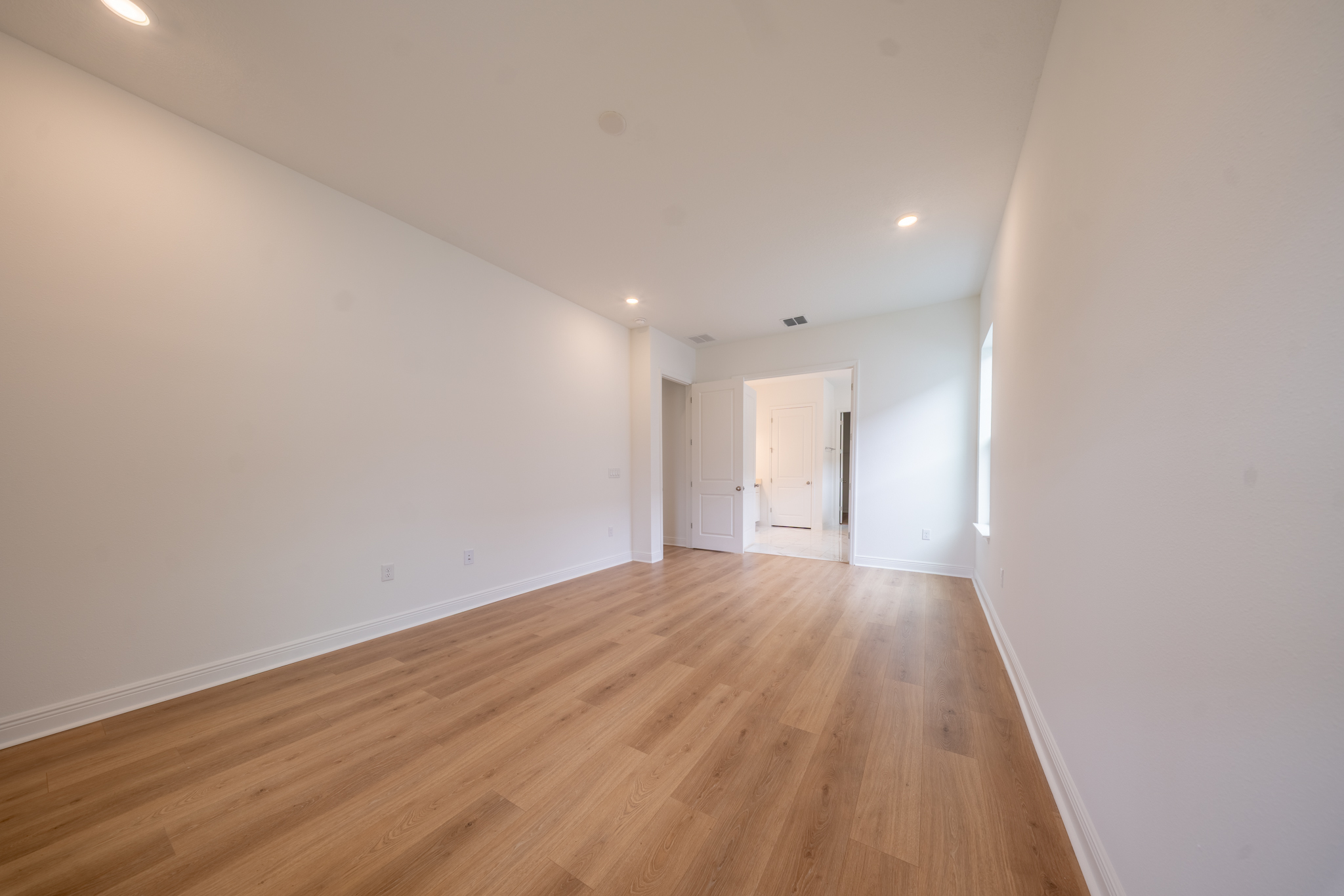 Empty primary bedroom with recessed lighting and door to en suite bathroom
