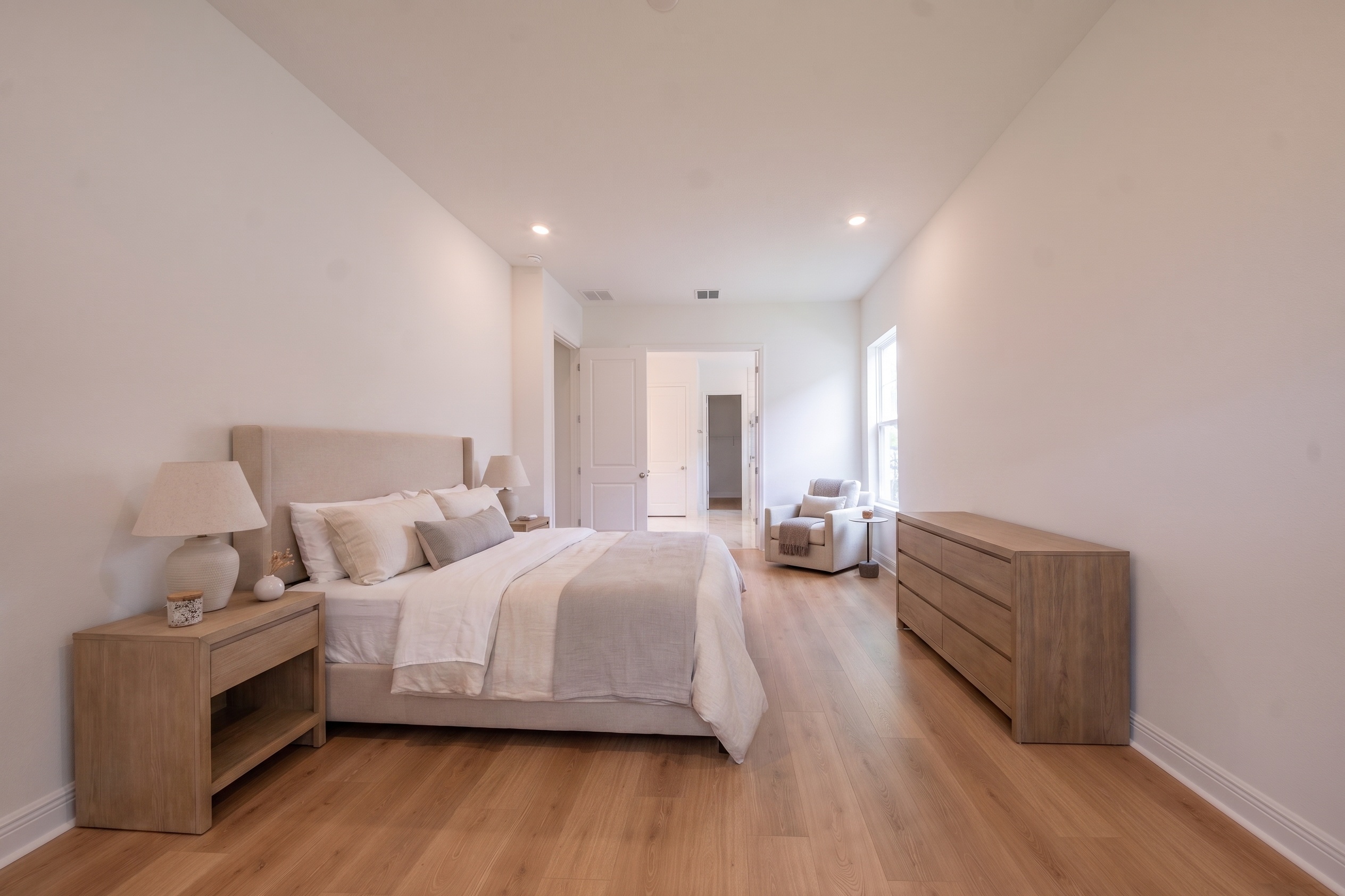 Virtually staged primary bedroom with upholstered king bed, wood nightstands, dresser and armchair