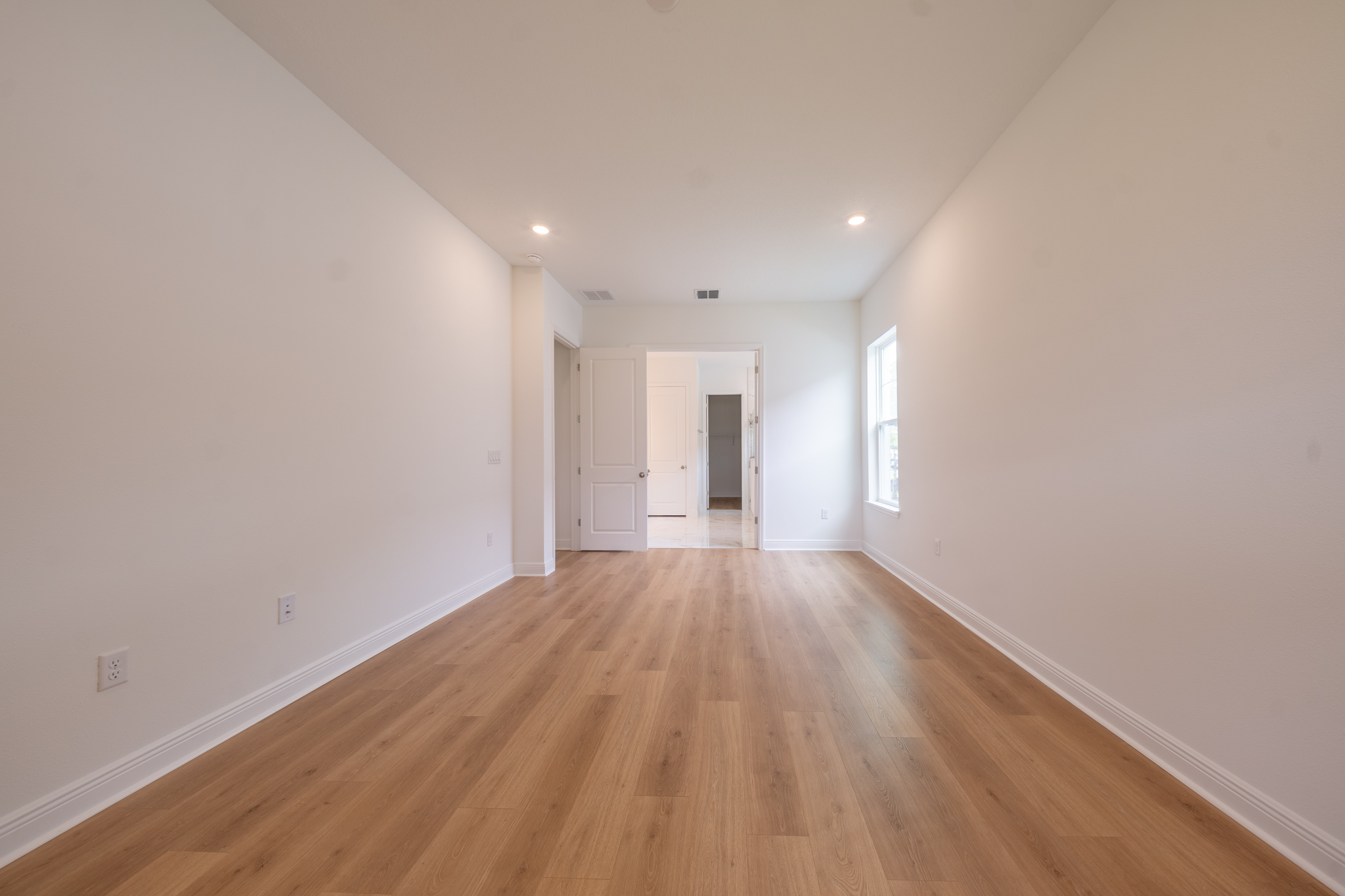 Empty bedroom with recessed lighting and hallway view