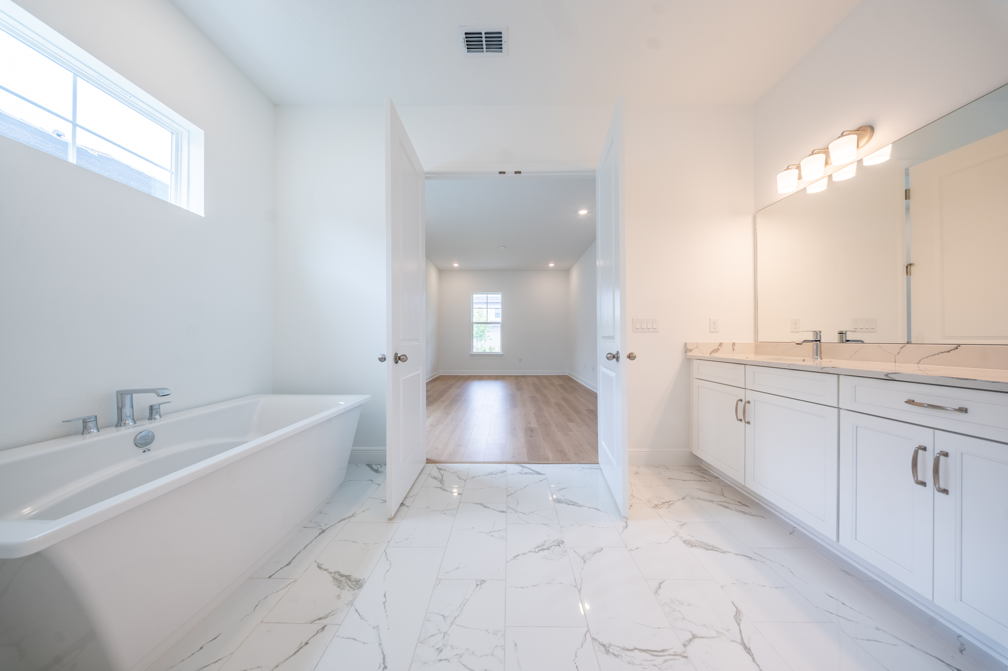 Primary bathroom with freestanding soaking tub, double vanity with quartz top and marble-look tile floor