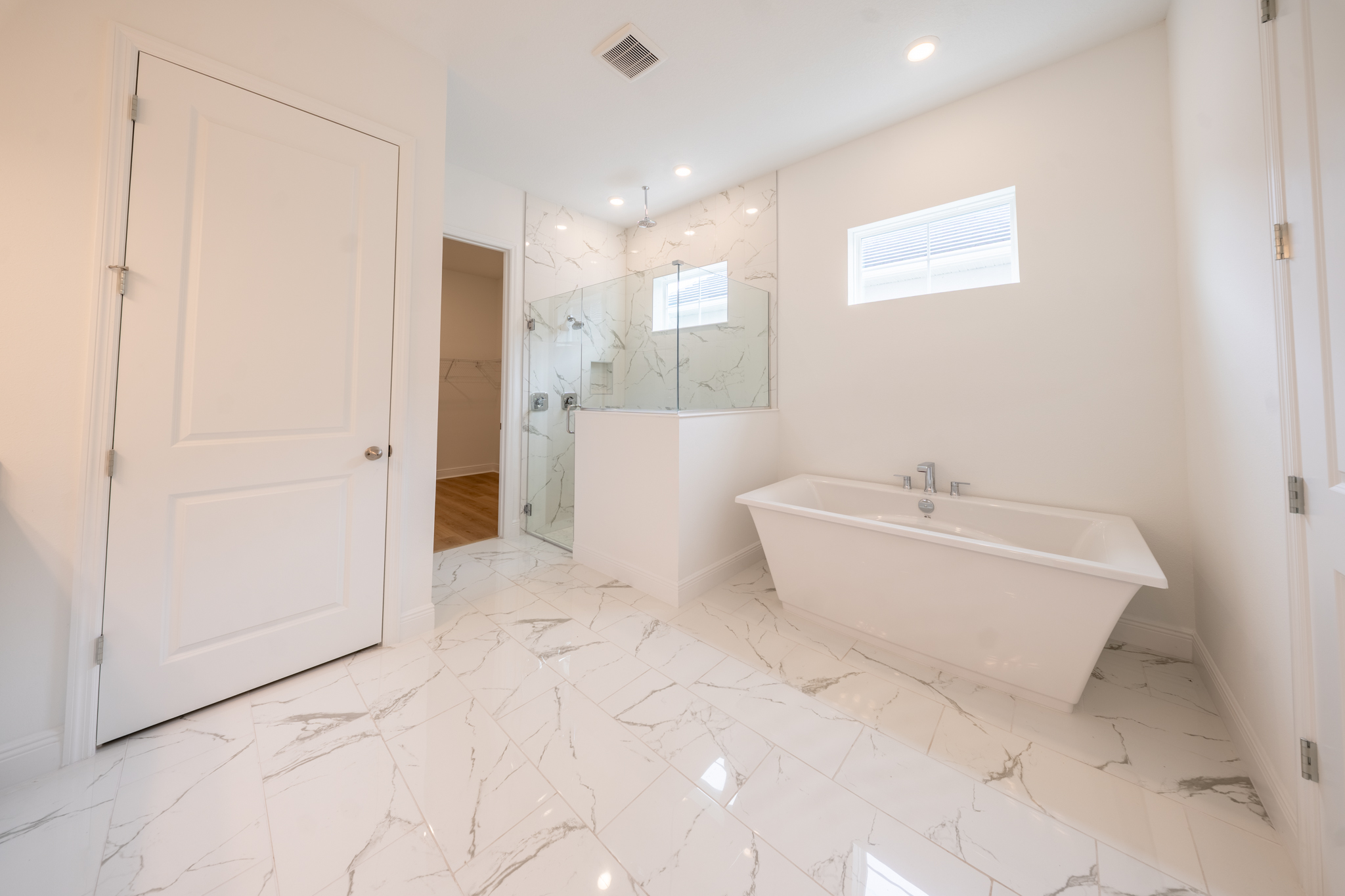Primary bathroom with freestanding soaking tub, frameless glass walk-in shower and marble tile