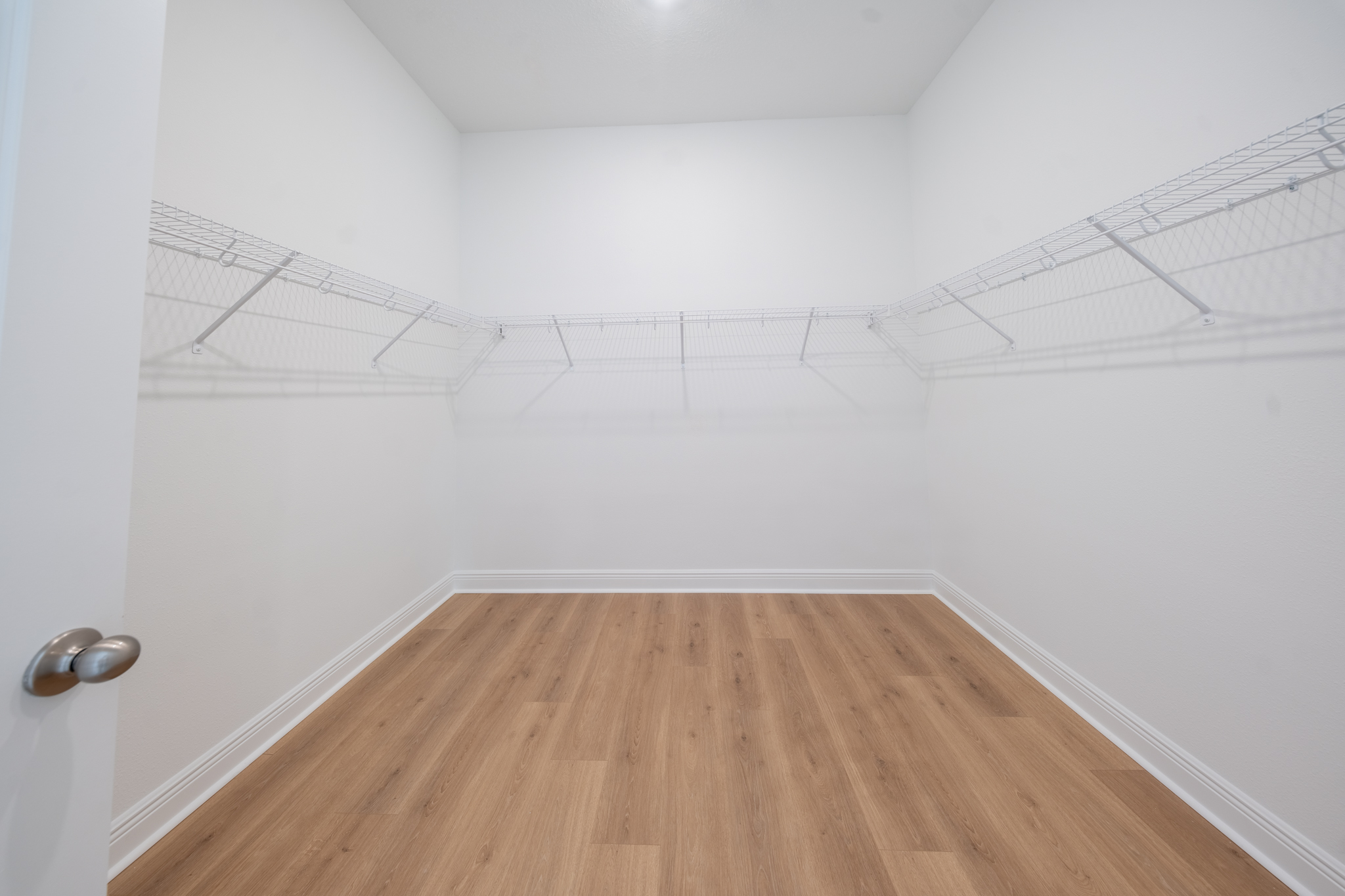 Spacious walk-in closet with wire shelving and light hardwood floors
