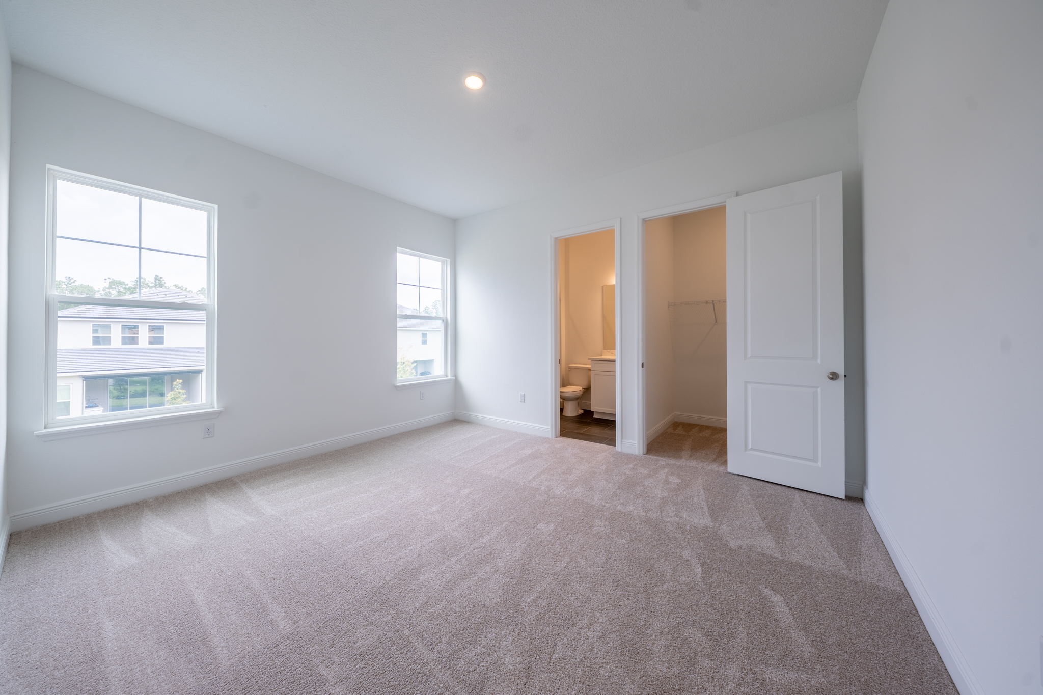 Empty carpeted bedroom with three windows and en suite bathroom door