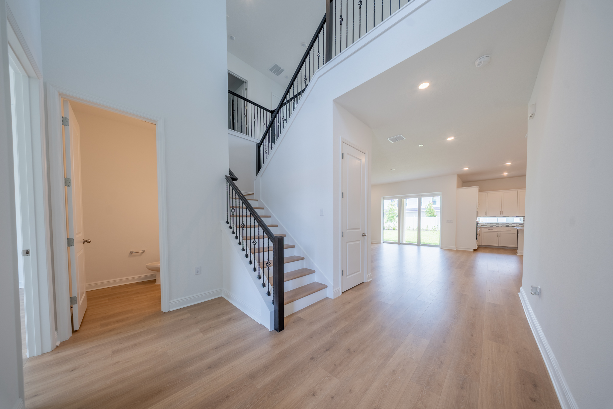 Two-story foyer with iron-railed staircase, half bath, and open view to living room and kitchen
