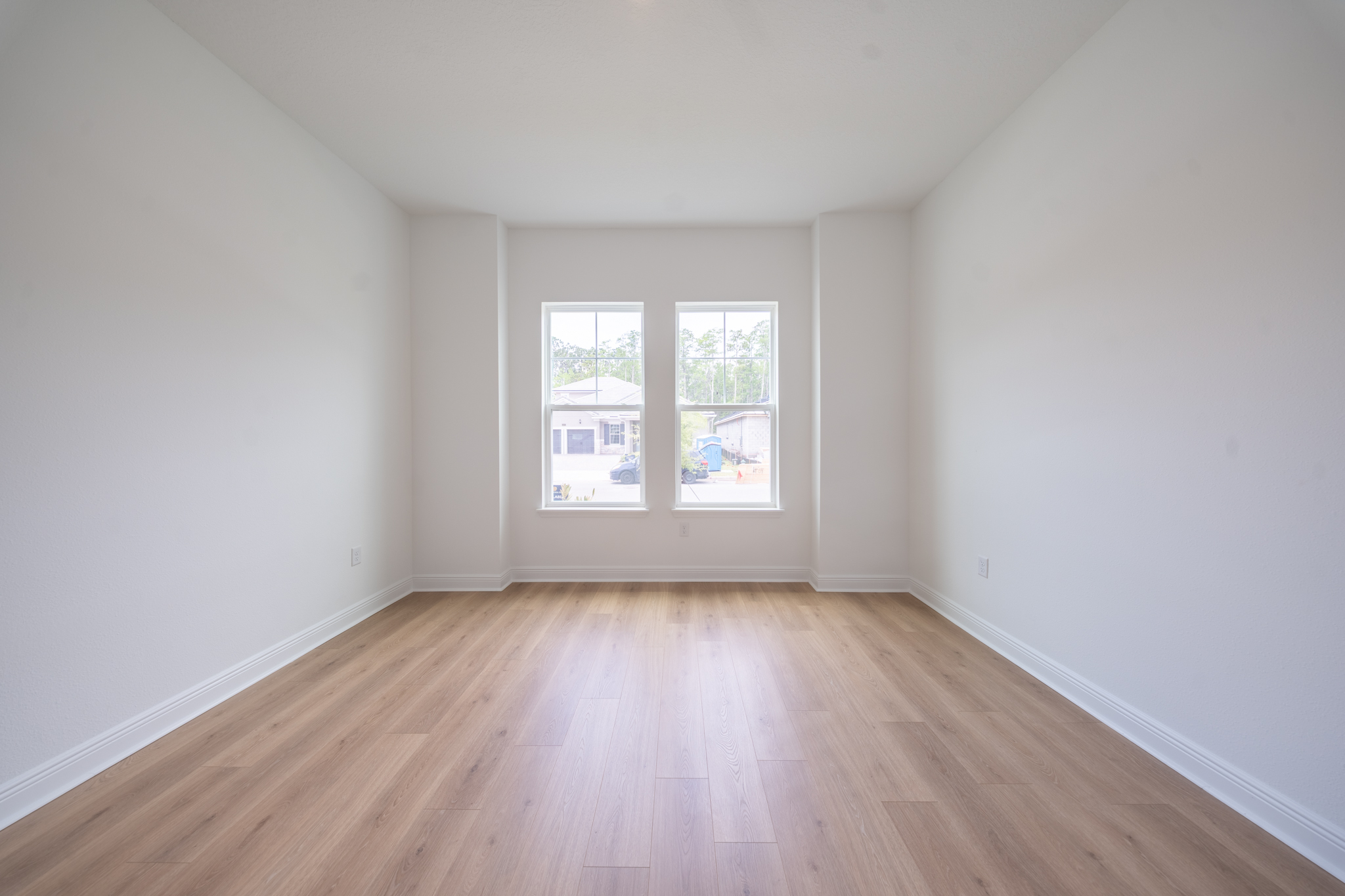 Empty bedroom with two windows and light hardwood floors