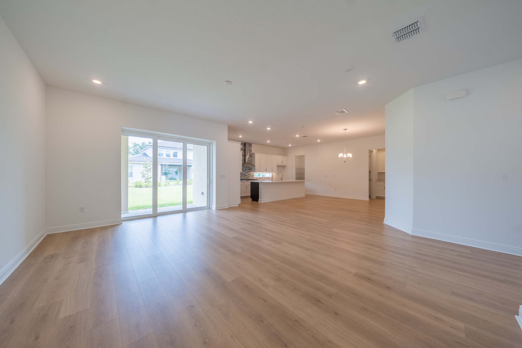 Open-plan living room with sliding glass doors to backyard and kitchen in background