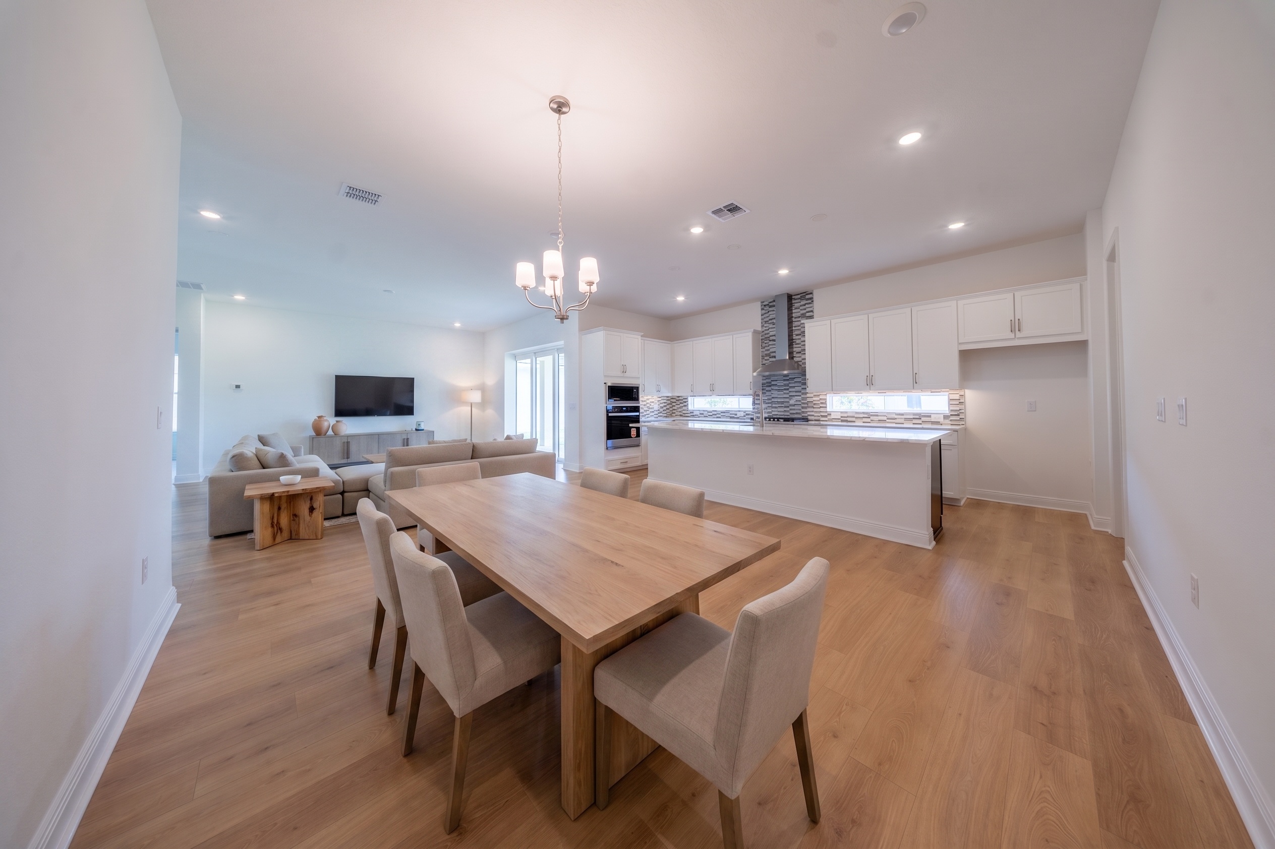 Virtually staged open-plan dining and living room with wood table, sectional sofa and kitchen in background