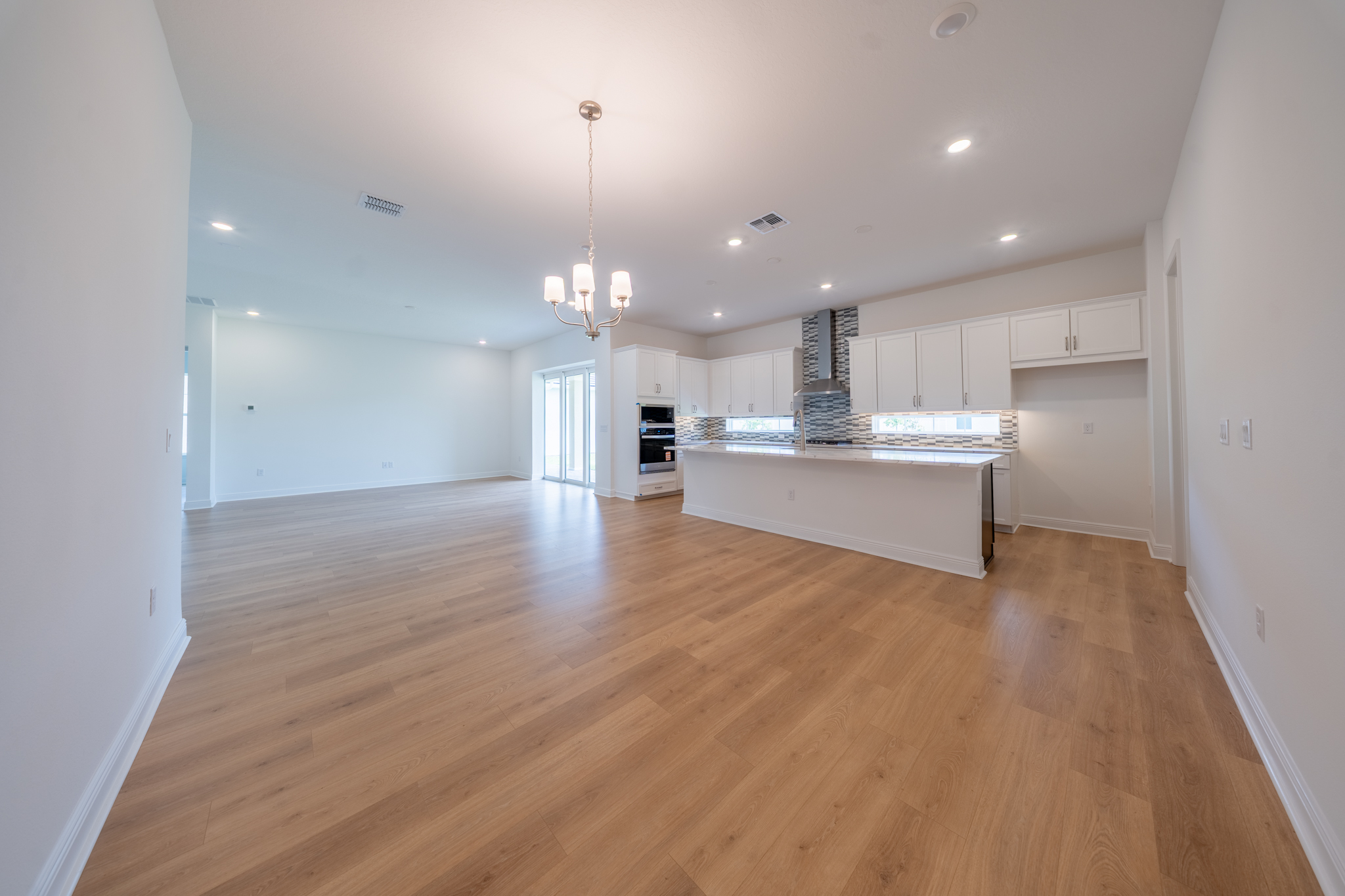 Dining area with chandelier, white shaker kitchen with dark island and sliding doors in background