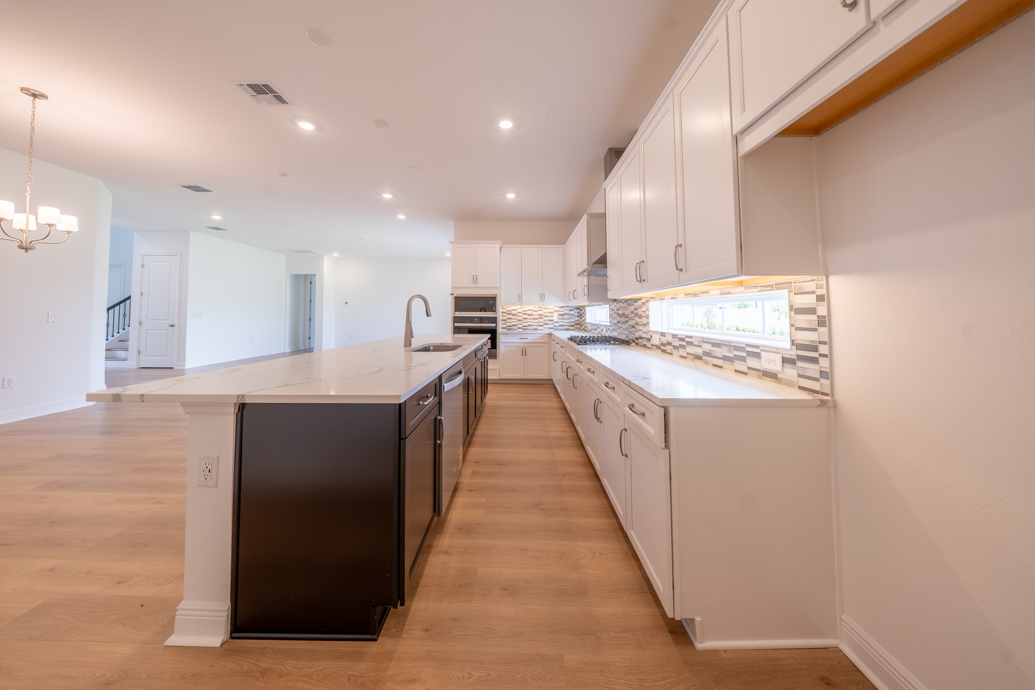 Kitchen with large dark island, quartz countertops, white shaker cabinets and stainless appliances