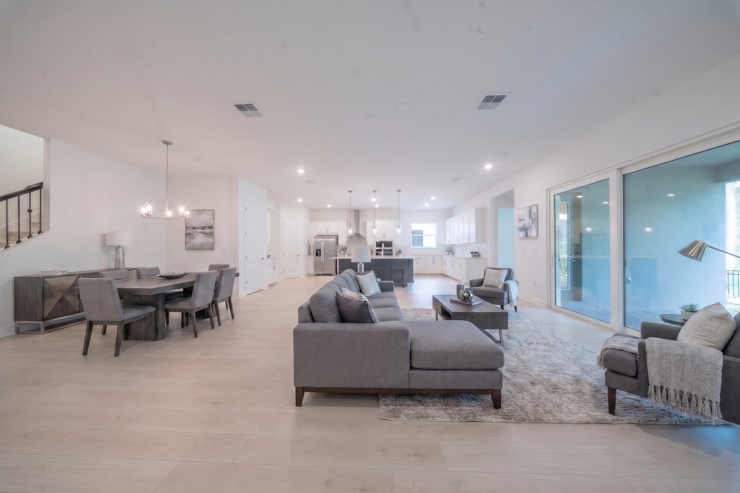 Virtually staged open-plan living and dining room with gray sectional, dining table and view to kitchen