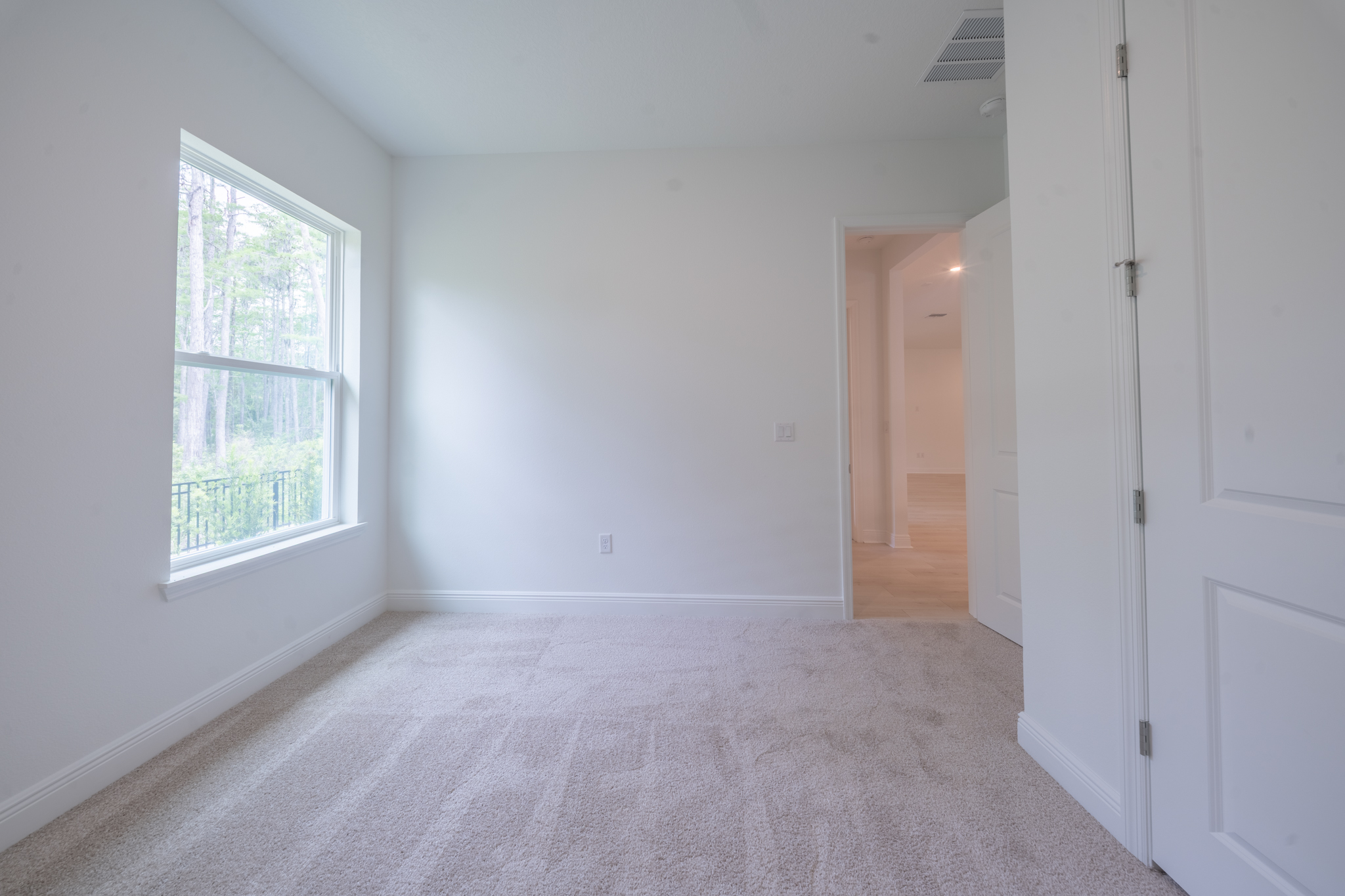 Carpeted bedroom with large window overlooking tree line and patio railing