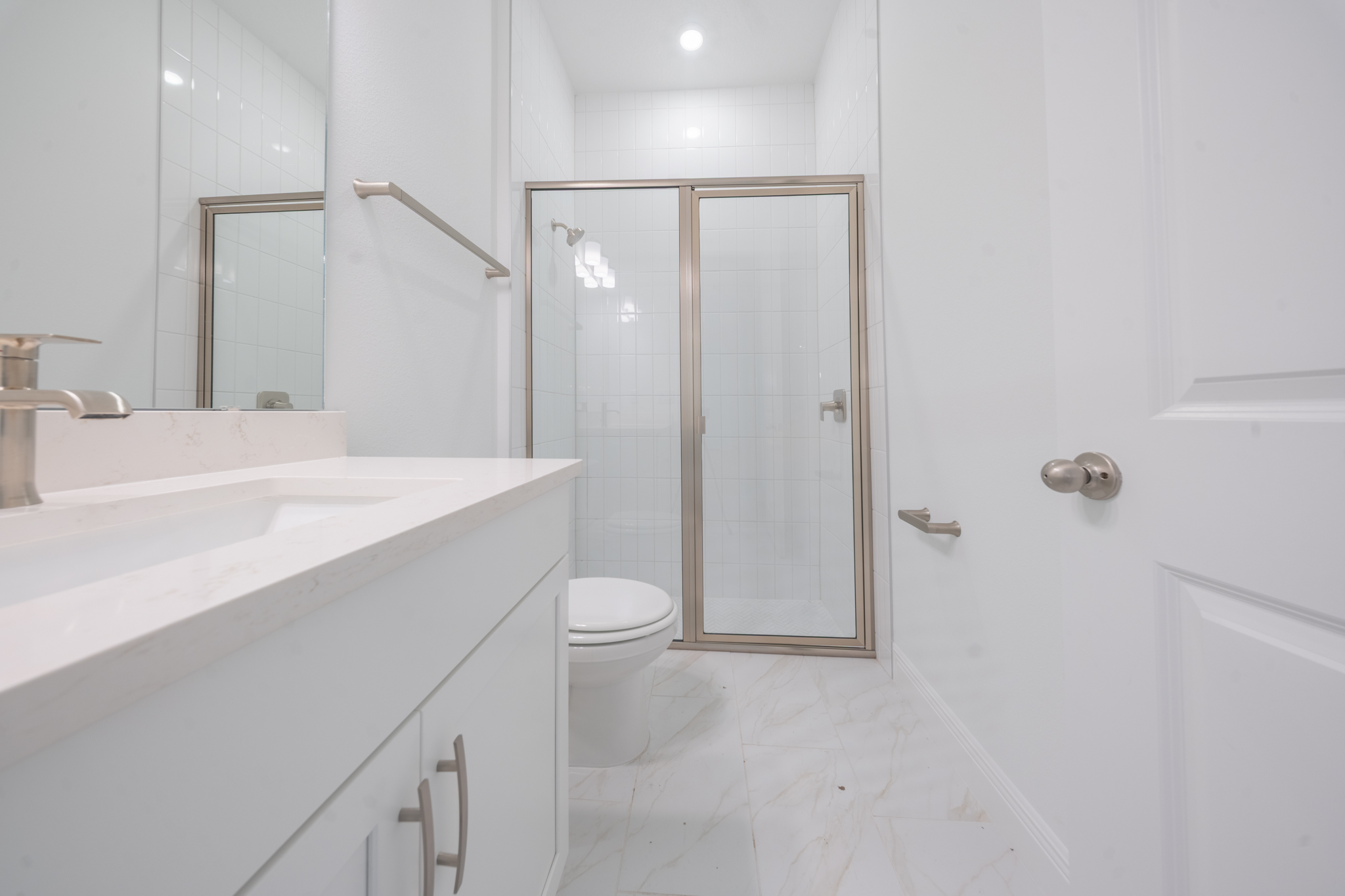 Bathroom with single vanity, quartz countertop and glass shower with white square tile