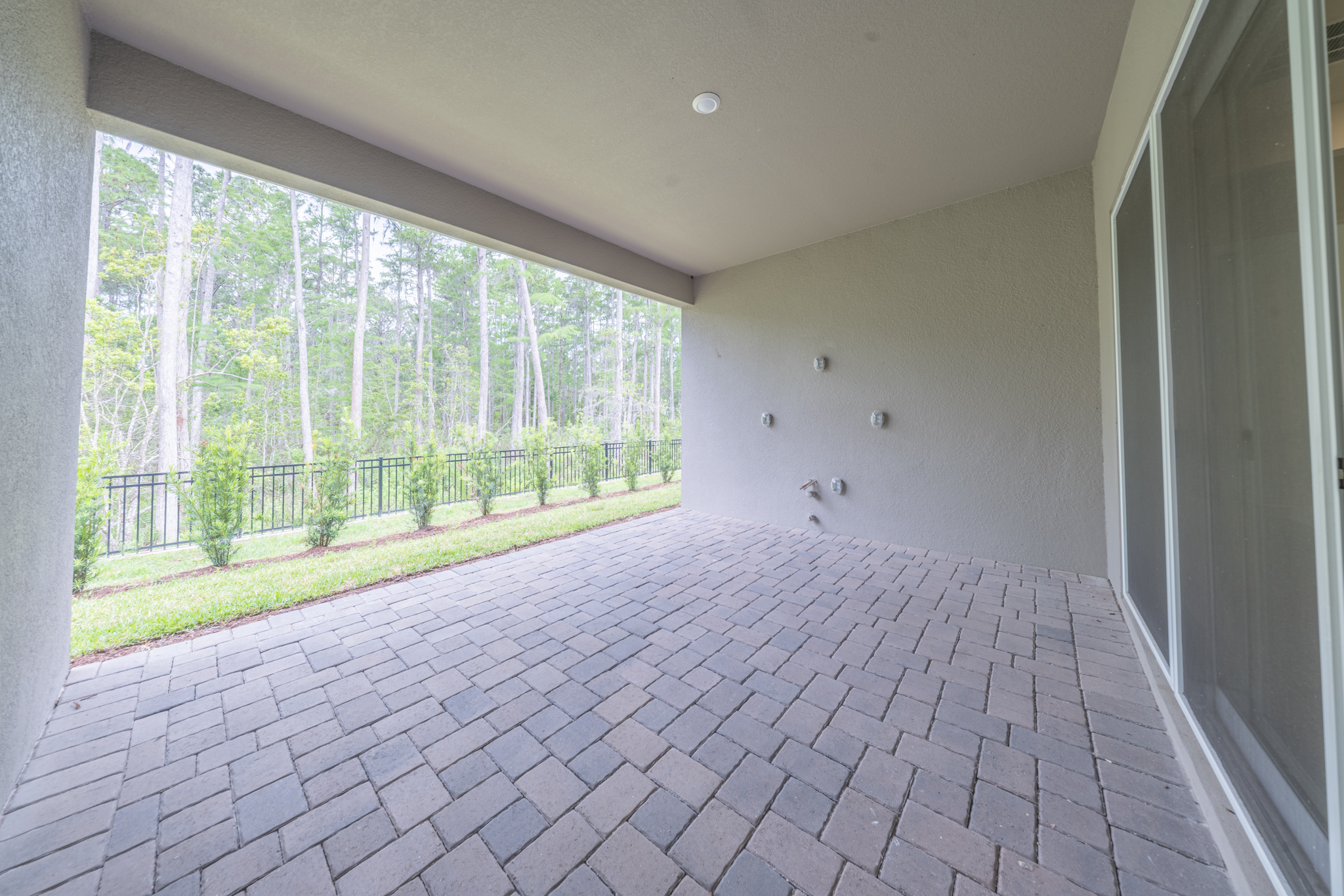 Covered paver patio with views to fenced backyard and mature tree line