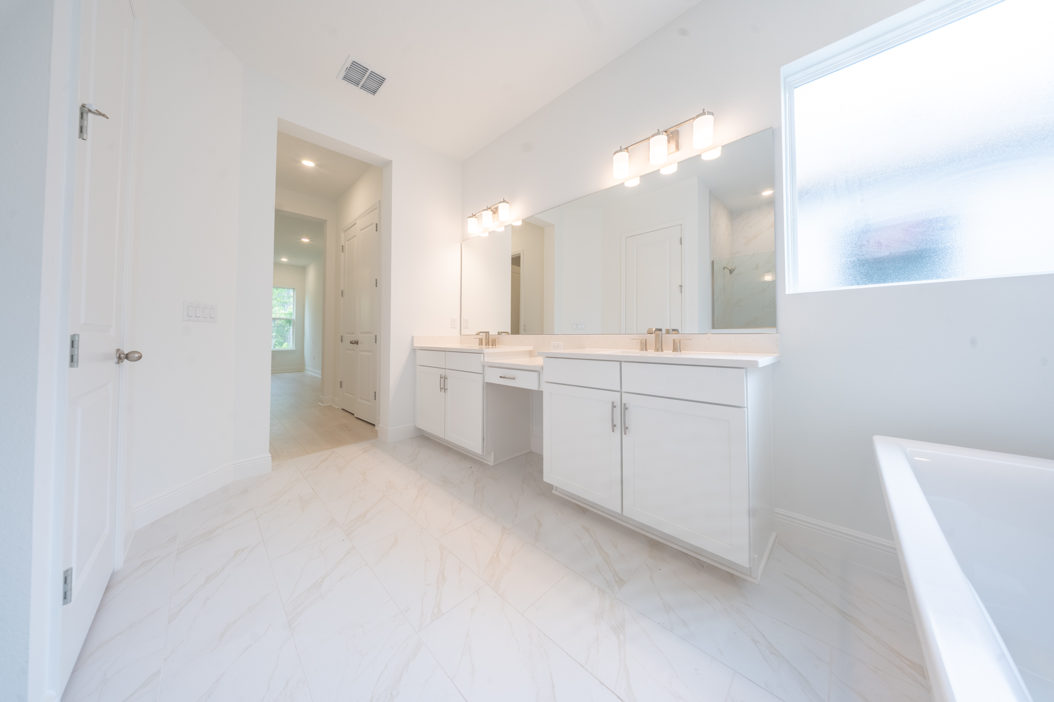 Primary bathroom with double vanity, dual mirrors, makeup counter and marble-look tile floor