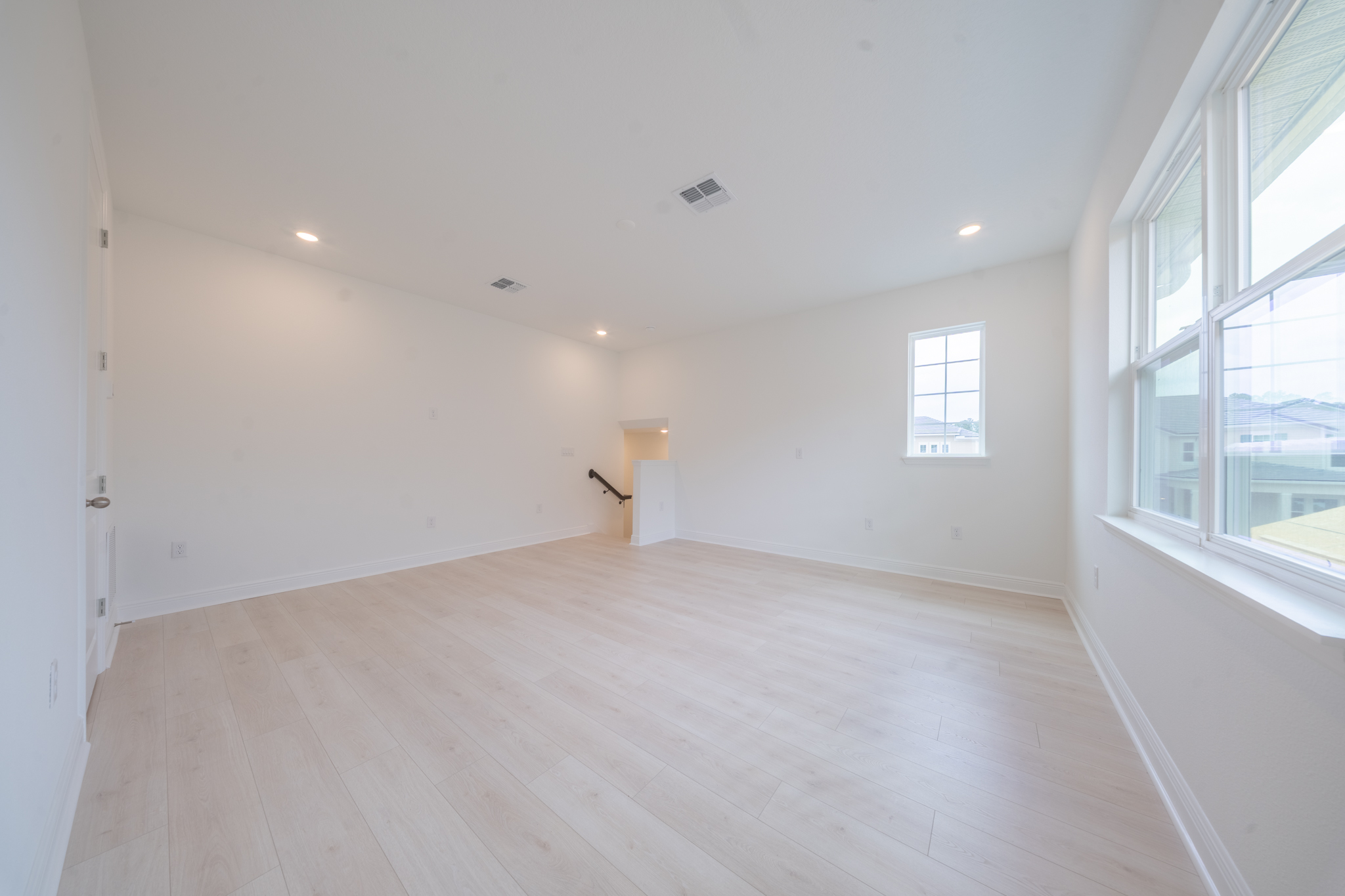 Upstairs loft with light hardwood floors, two windows and staircase railing