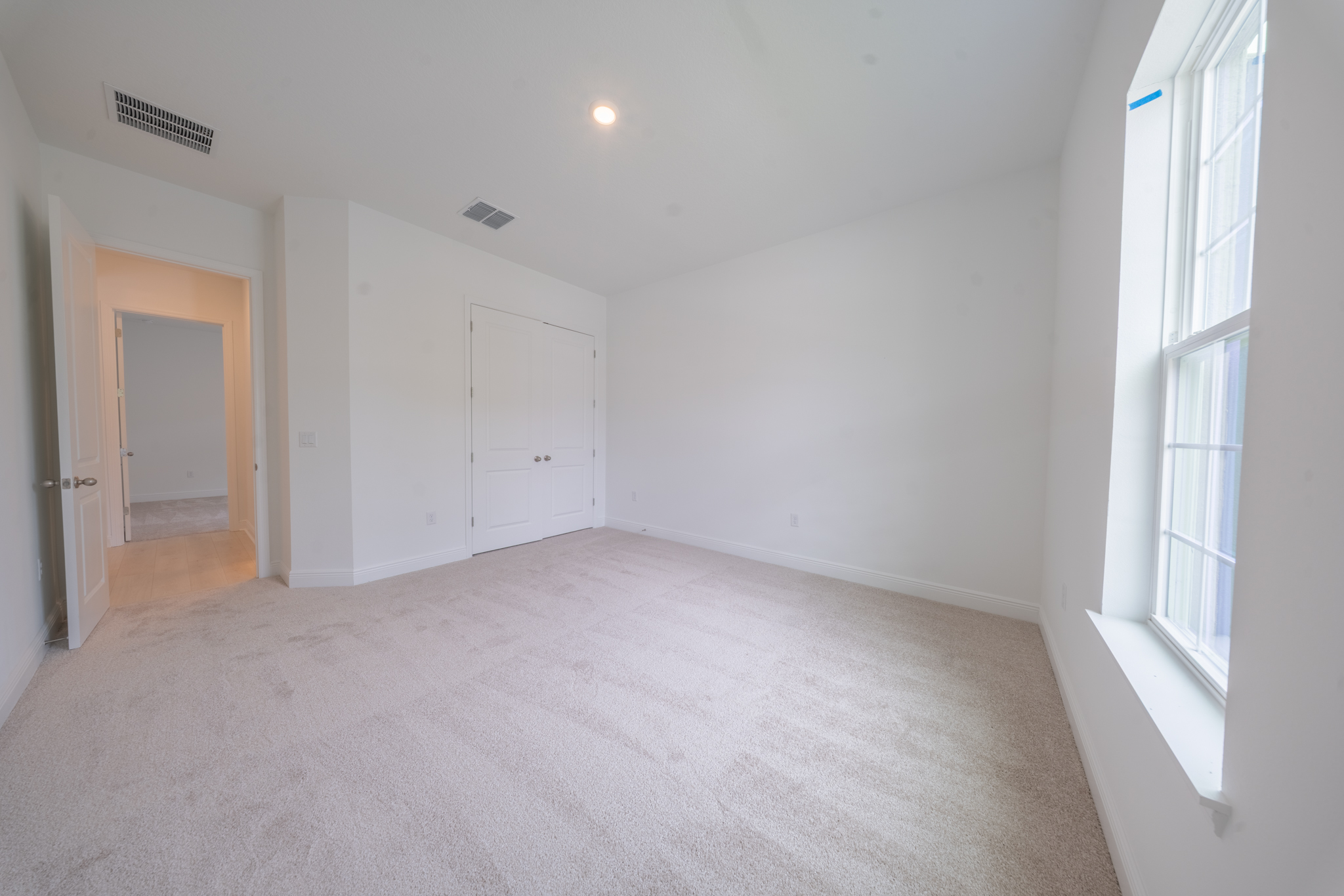 Empty carpeted bedroom with window, closet door and en suite bathroom entrance