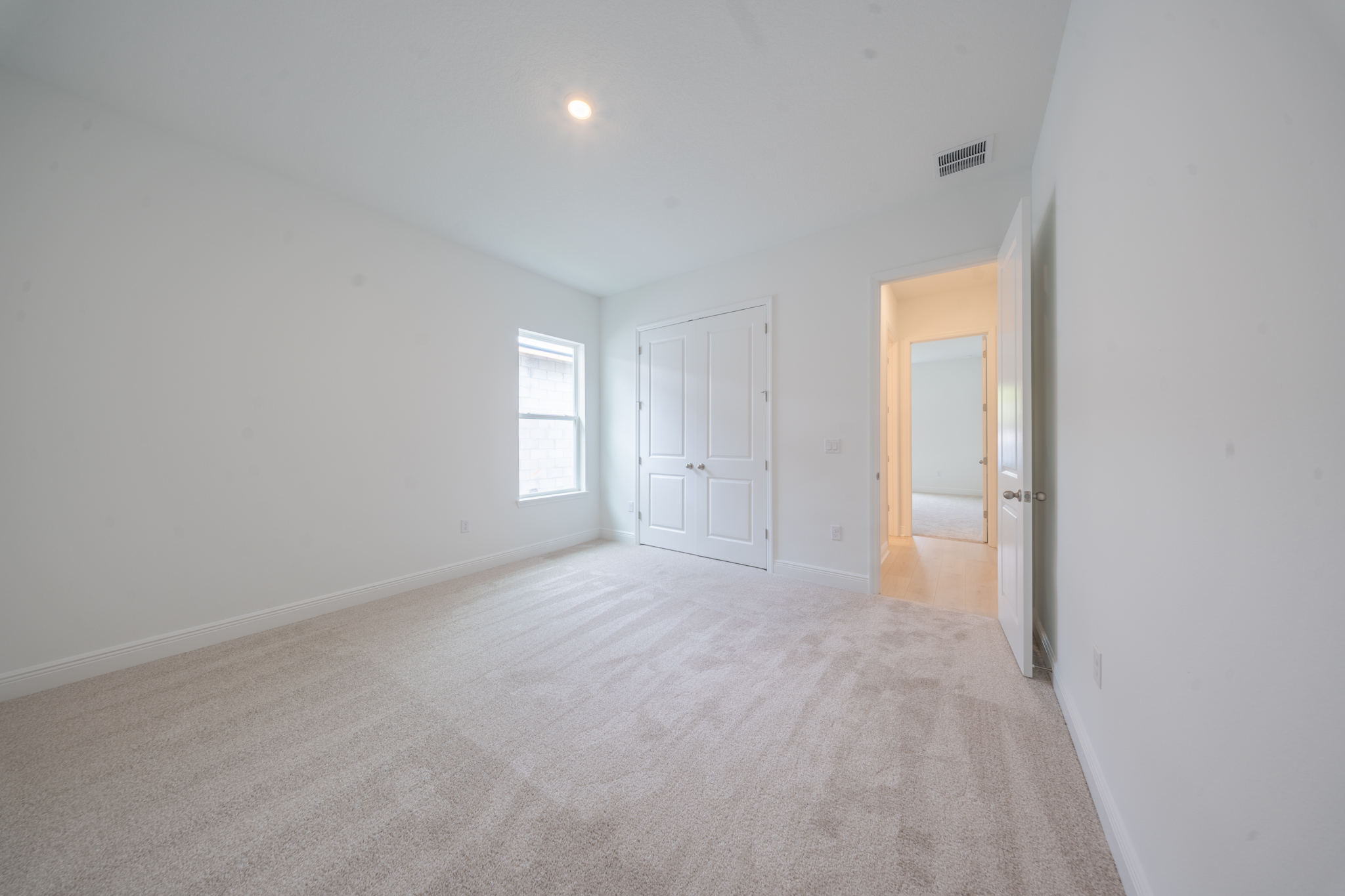 Empty carpeted bedroom with single window and double-door closet