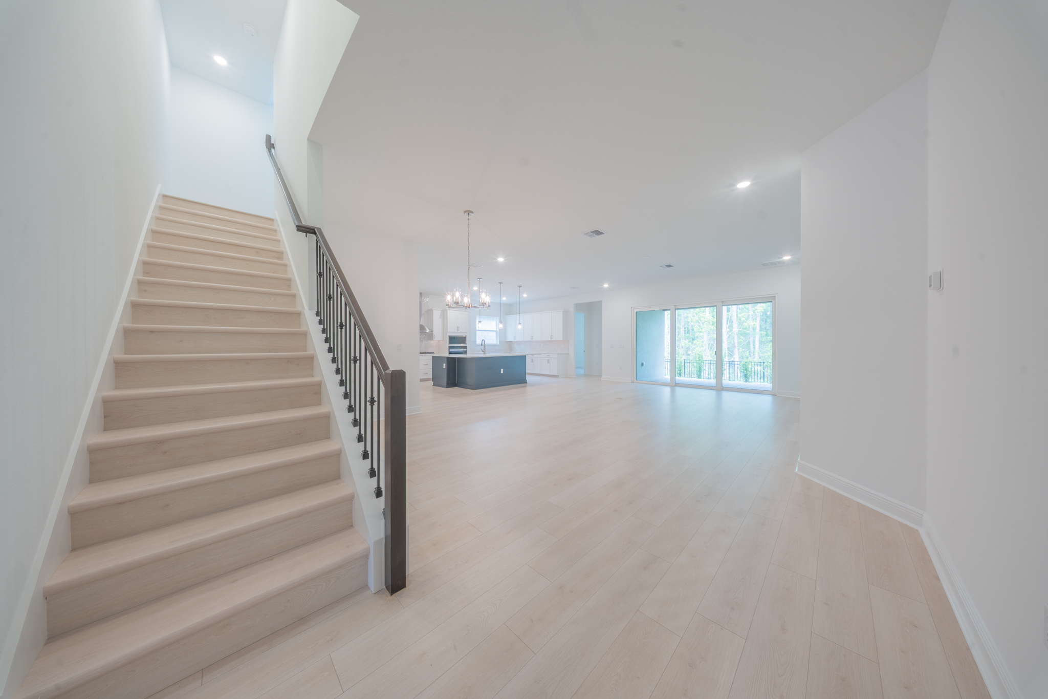 Open-plan living area with staircase, navy kitchen island in background and sliding doors to yard