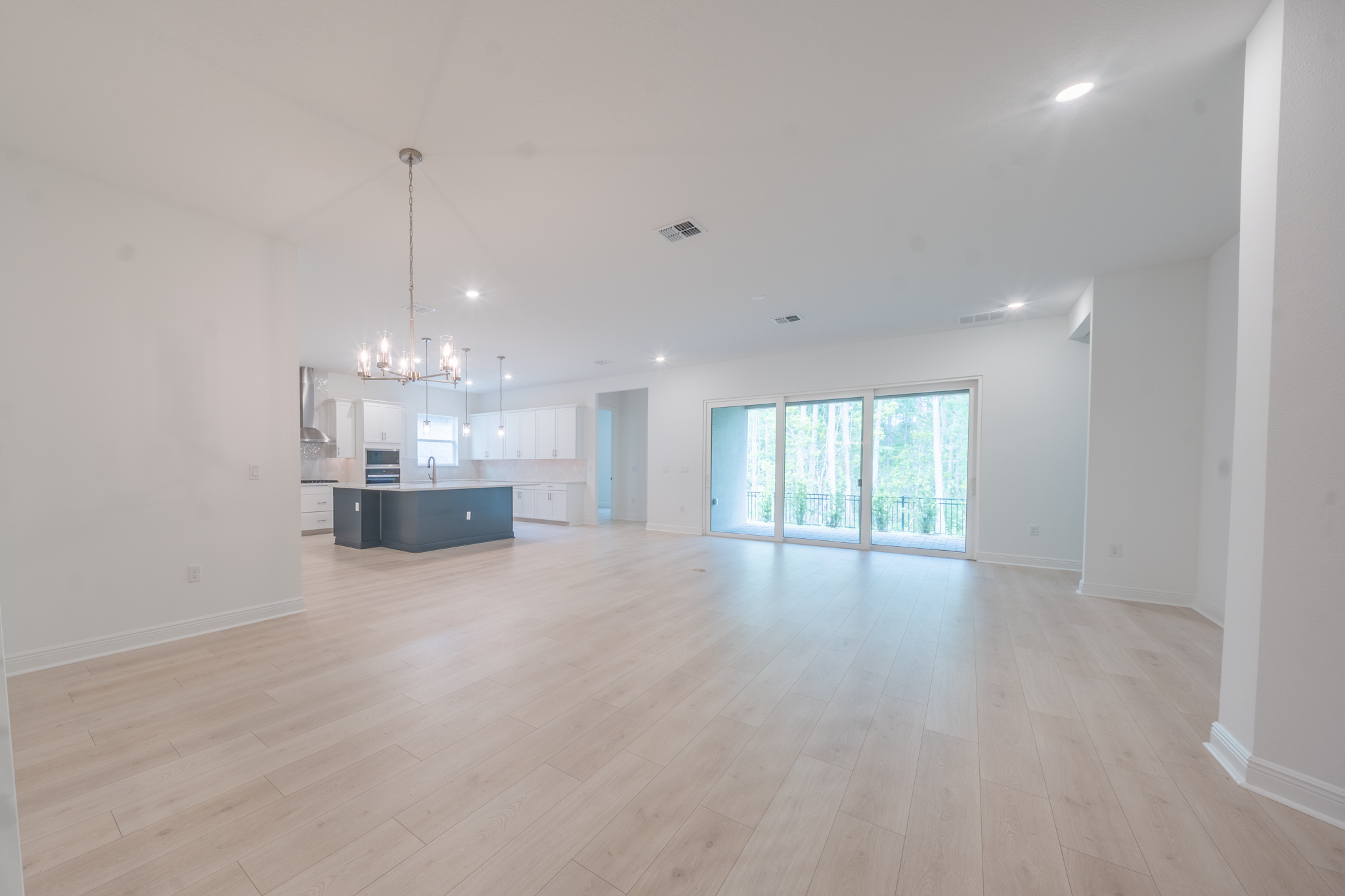 Spacious open-plan living and dining with chandelier, navy kitchen island and sliding doors to backyard