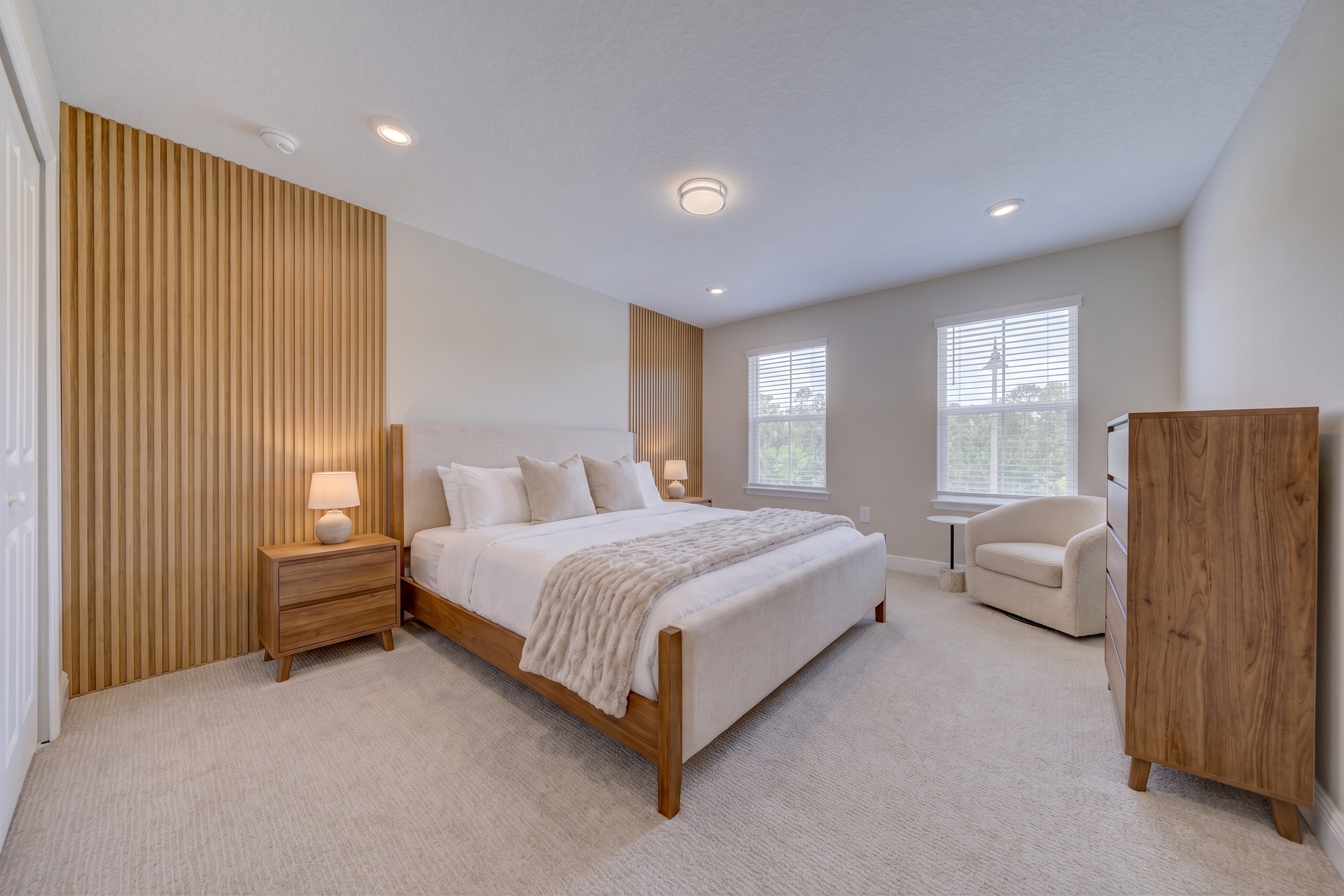 Virtually staged primary bedroom with wood platform king bed, matching nightstands, dresser and armchair