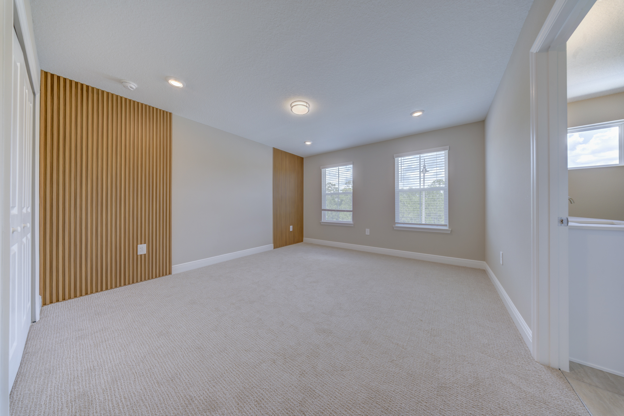 Empty primary bedroom with full-height wood slat accent wall, two windows and en suite entrance