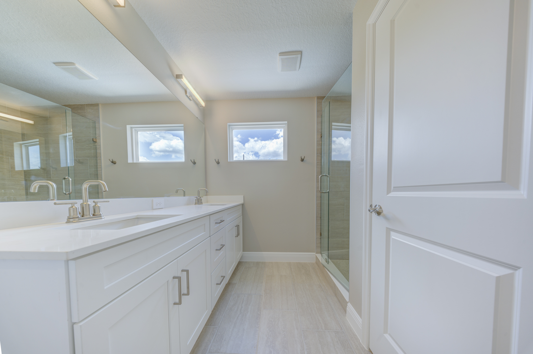 Primary bathroom with double white vanity, quartz countertop, large mirror and frameless glass walk-in shower