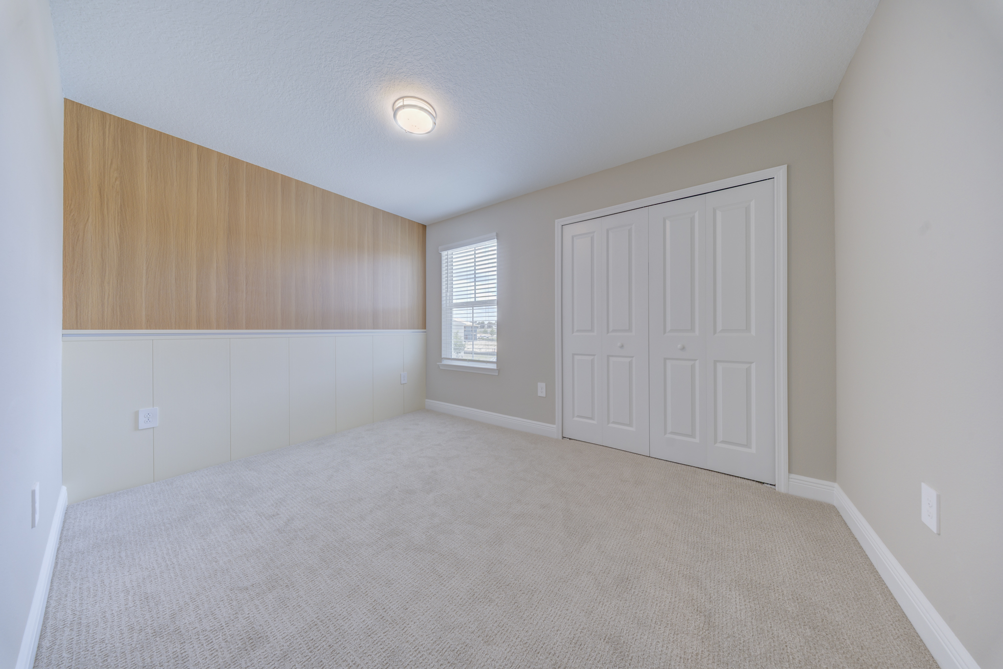 Empty bedroom with wood wainscoting accent wall, double-door closet and single window