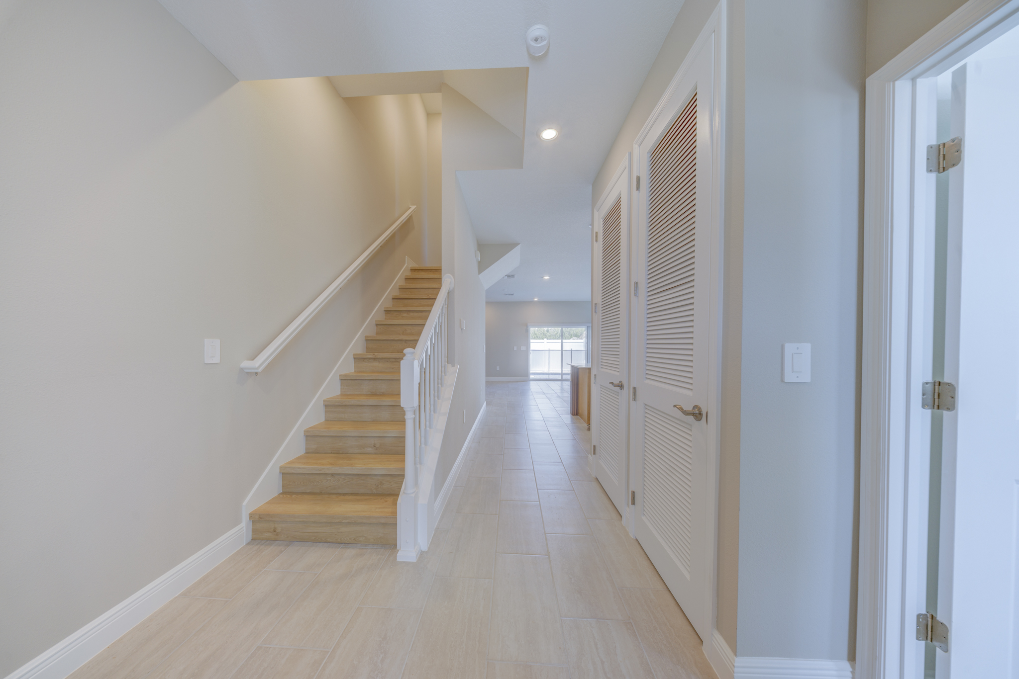 Entry foyer with open staircase, louvered closet doors and view to open-plan living area