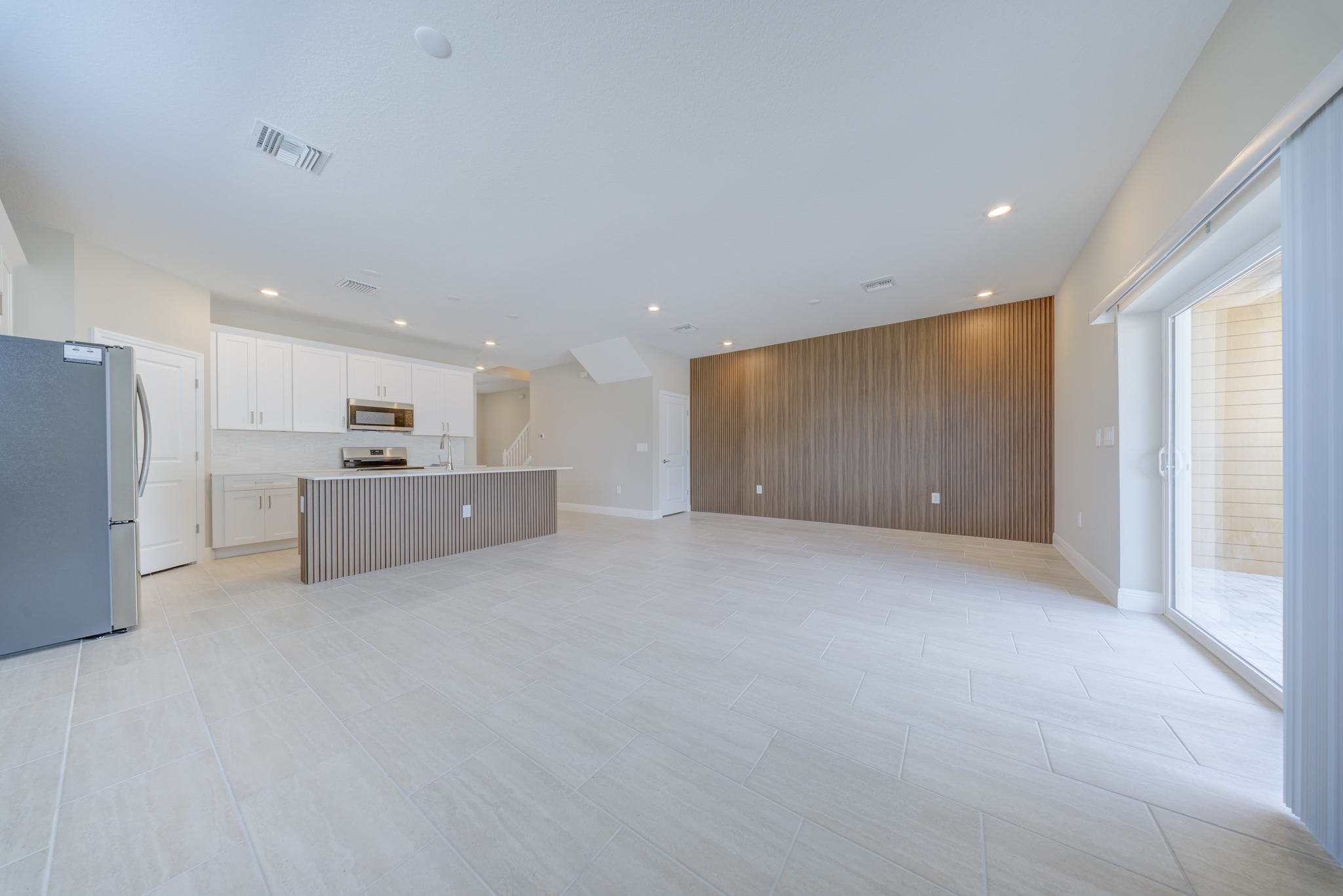 Empty open-plan living and dining area with wood slat feature wall, kitchen island and large sliding glass door
