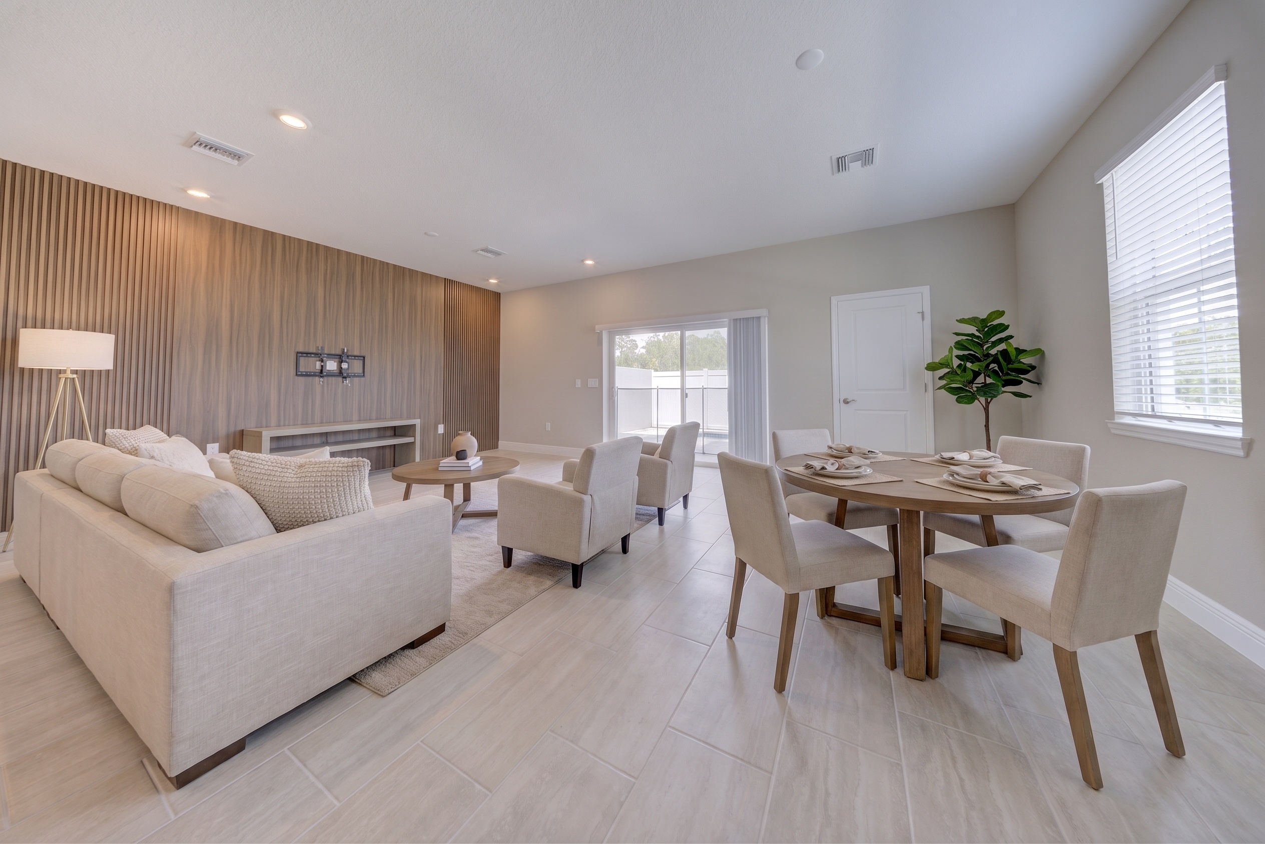 Virtually staged living and dining room with cream sofa, TV mount on wood slat wall, round dining table and fiddle-leaf fig