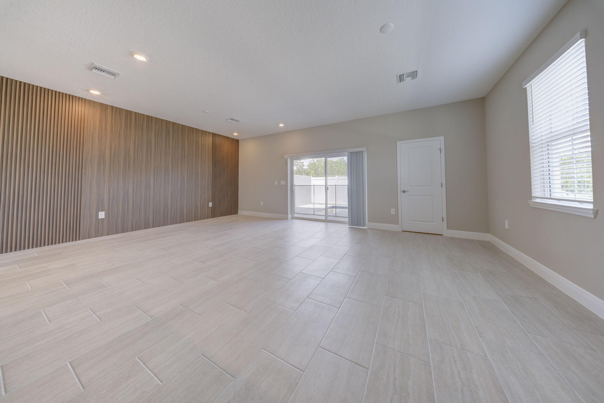 Empty living room with floor-to-ceiling wood slat accent wall and sliding glass door to pool