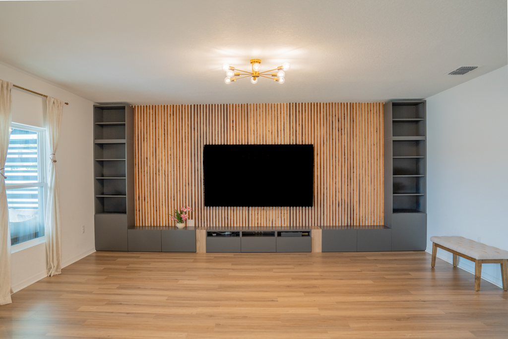 Living room feature wall with wood slat accent, large TV and built-in shelving