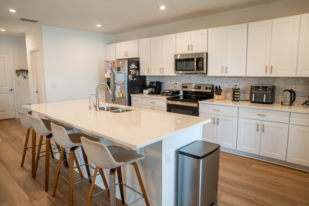 Kitchen with large white island, bar stools, stainless appliances and gray tile backsplash