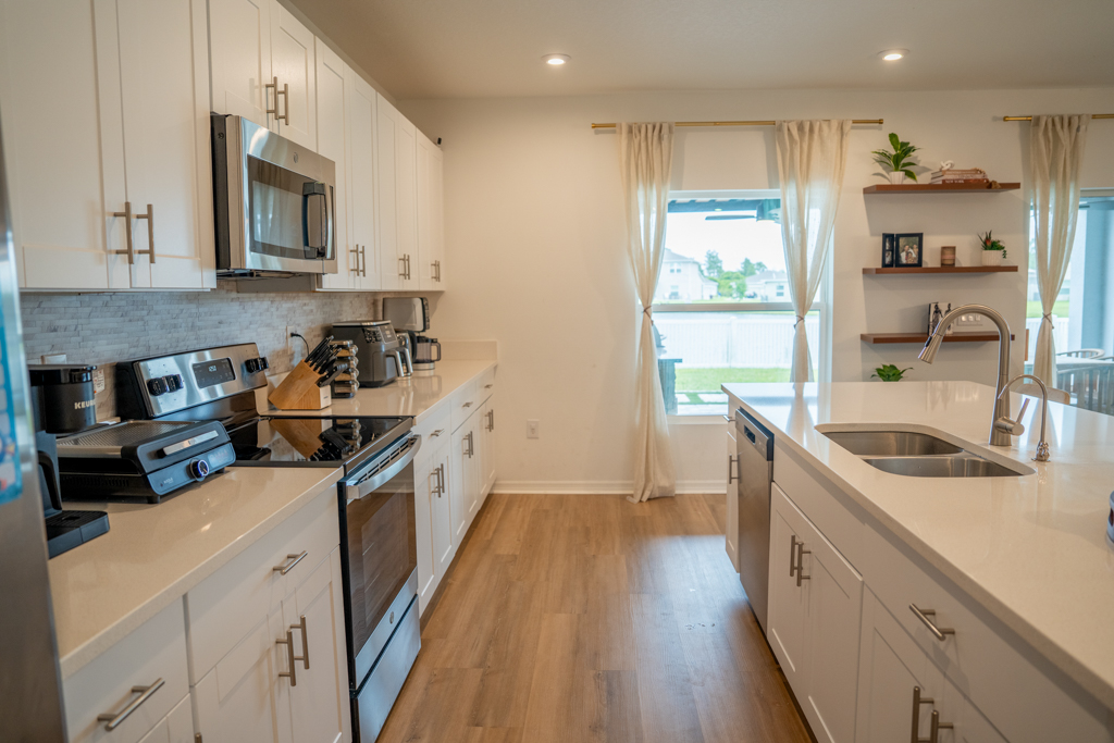 Kitchen with stainless range, white cabinets, gray tile backsplash and view to dining area
