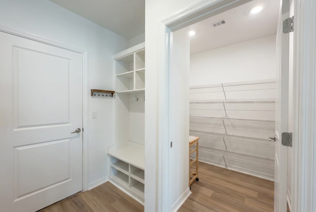 Virtually staged mudroom with built-in bench and cubbies beside empty walk-in pantry