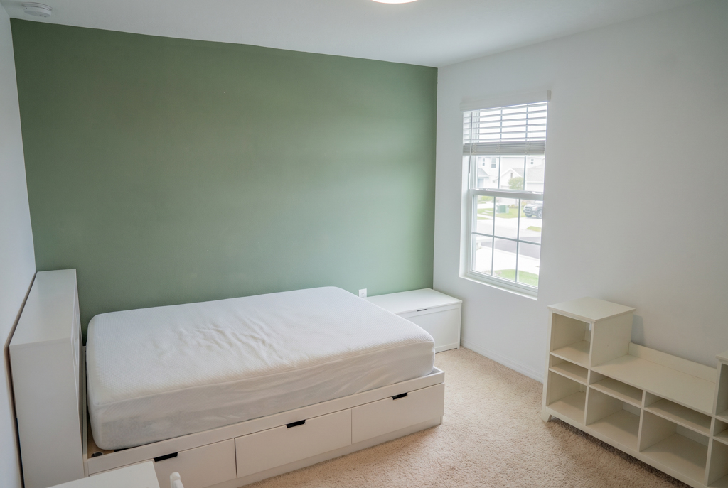 Virtually staged boy's bedroom with green accent wall and white platform bed