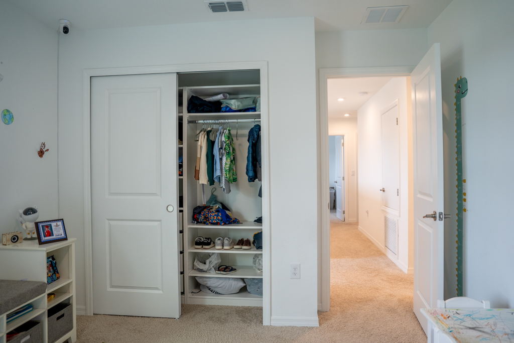 Boy's bedroom closet with hanging clothes and hallway view