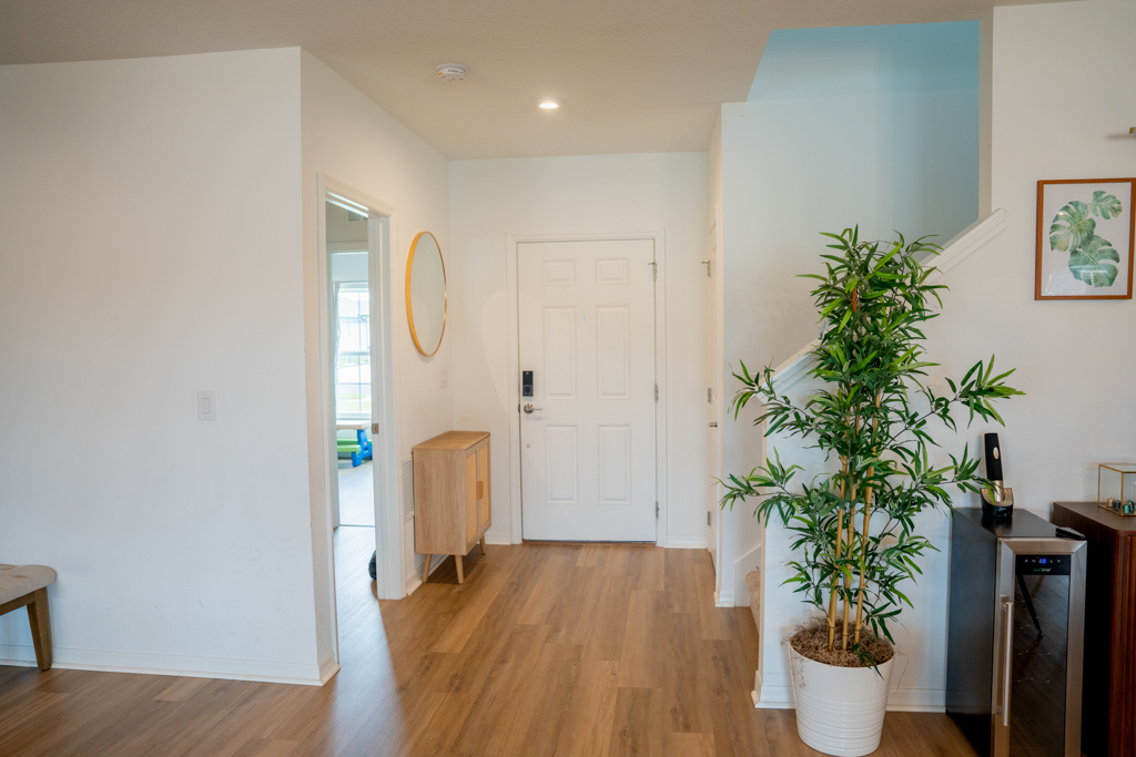 Foyer with front door, round mirror, bamboo plant and staircase