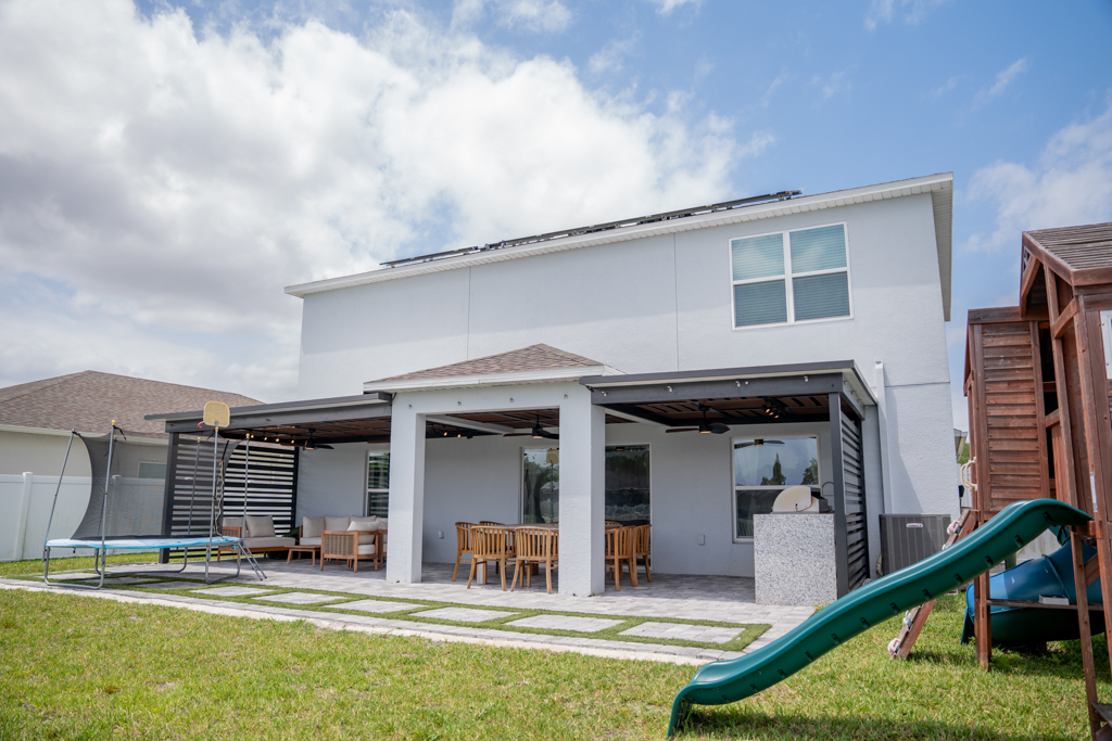 Rear exterior of home with modern pergola, outdoor dining, outdoor kitchen and playground