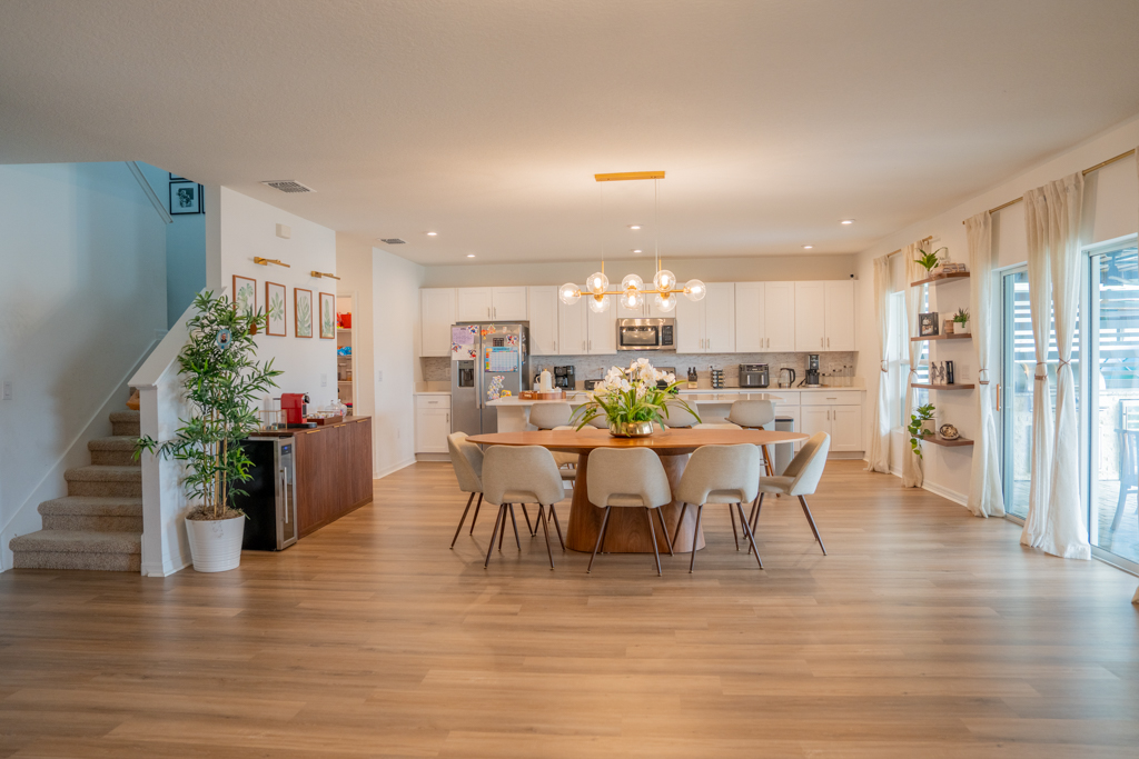 Open-plan dining area with oval wood table and white chairs, kitchen and living room in background