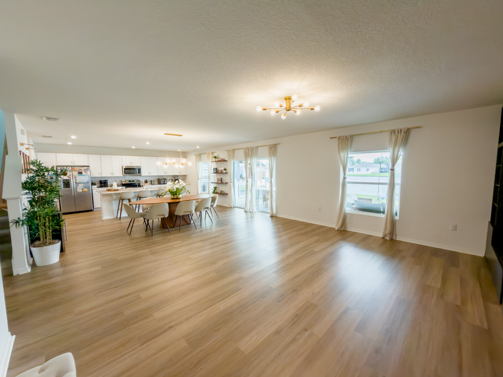Wide open-plan living and dining space with hardwood floors and kitchen in background