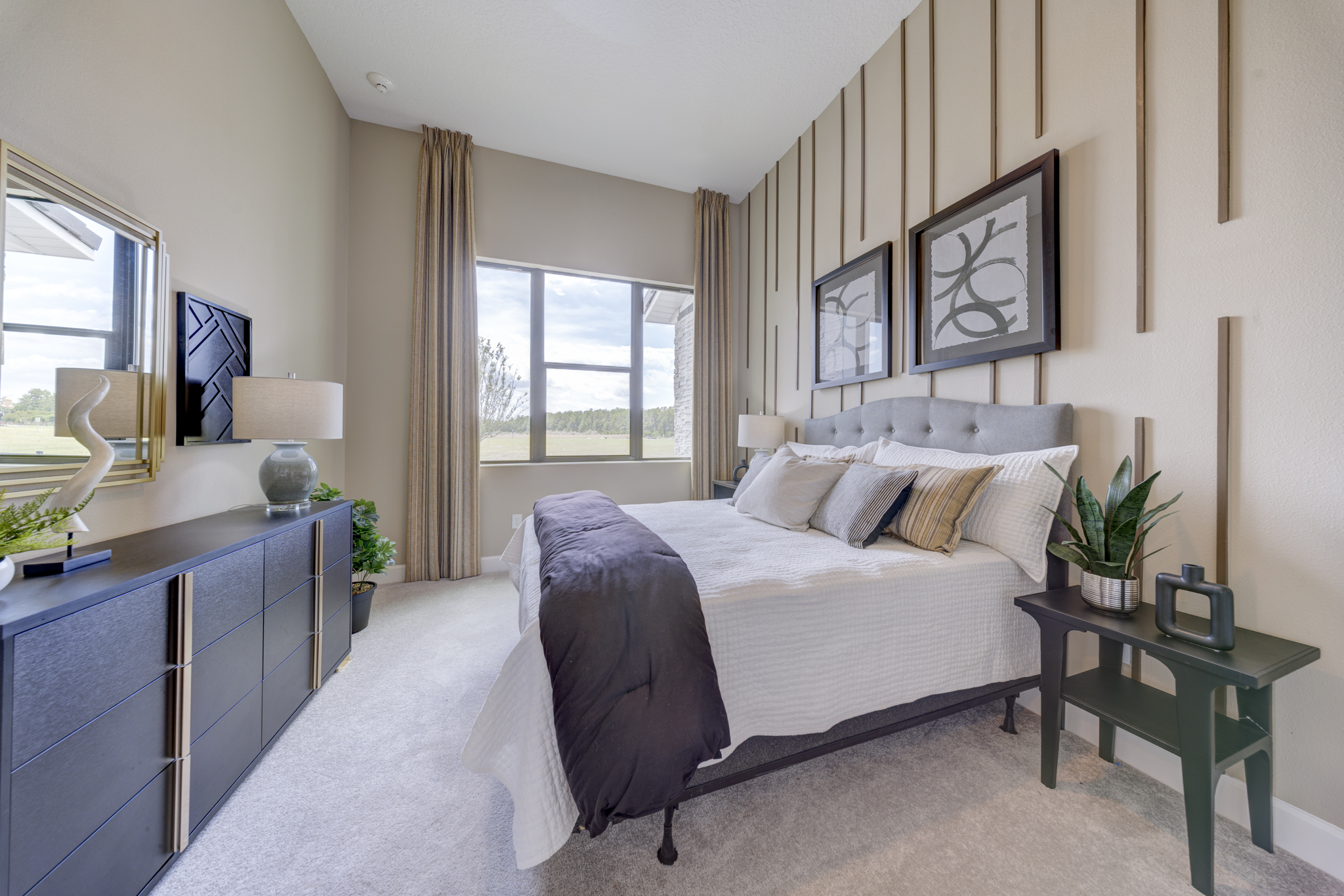 Guest bedroom with vertical striped accent wall, tufted upholstered queen bed, dark navy dresser and large windows